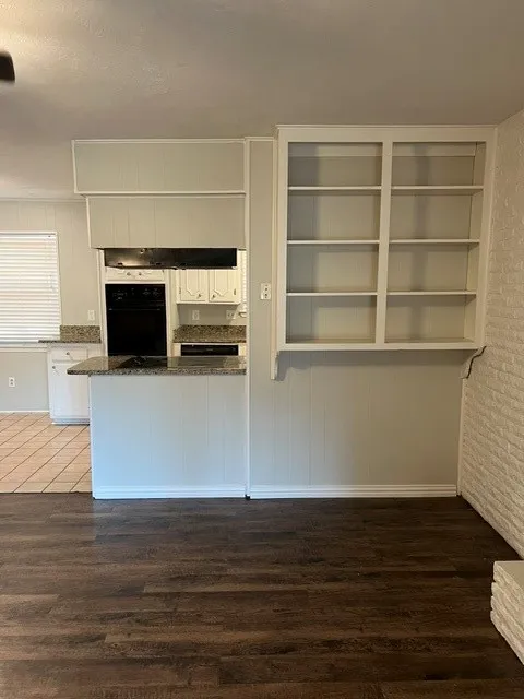 Wood-finish flooring, built-in shelving, white brick accent, granite countertops, and white cabinetry