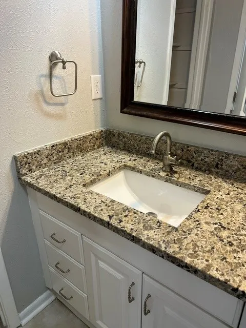 White vanity with brushed nickel hardware, undermount sink, and speckled countertop