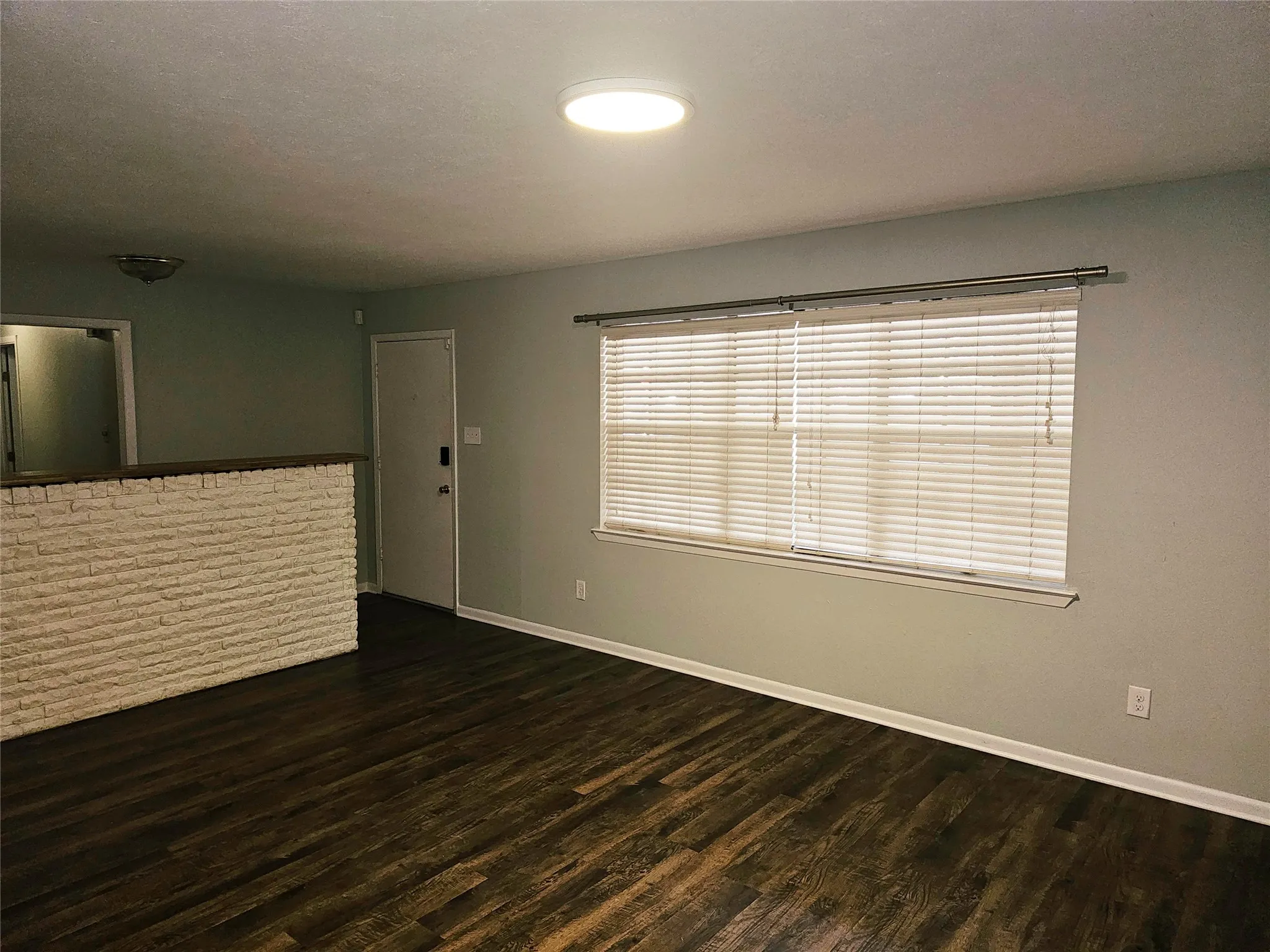 Wood-finish flooring, half-height decorative stone wall, window with blinds, flush-mount ceiling light