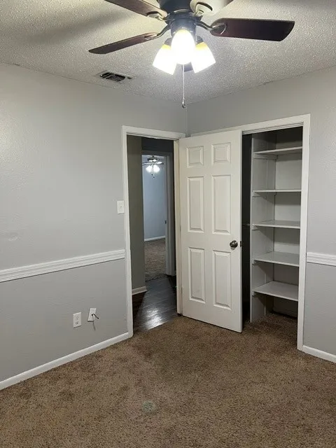 Textured carpet flooring, neutral paint palette, ceiling fan with integrated lighting, built-in shelving, and panel doors
