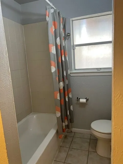 Bathroom featuring a built-in tub with tile surround, a window with frosted glass, and tiled flooring