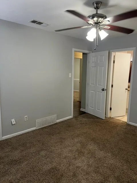 Plush carpet flooring, light-toned wall finishes, ceiling fan with integrated lighting, and white trim