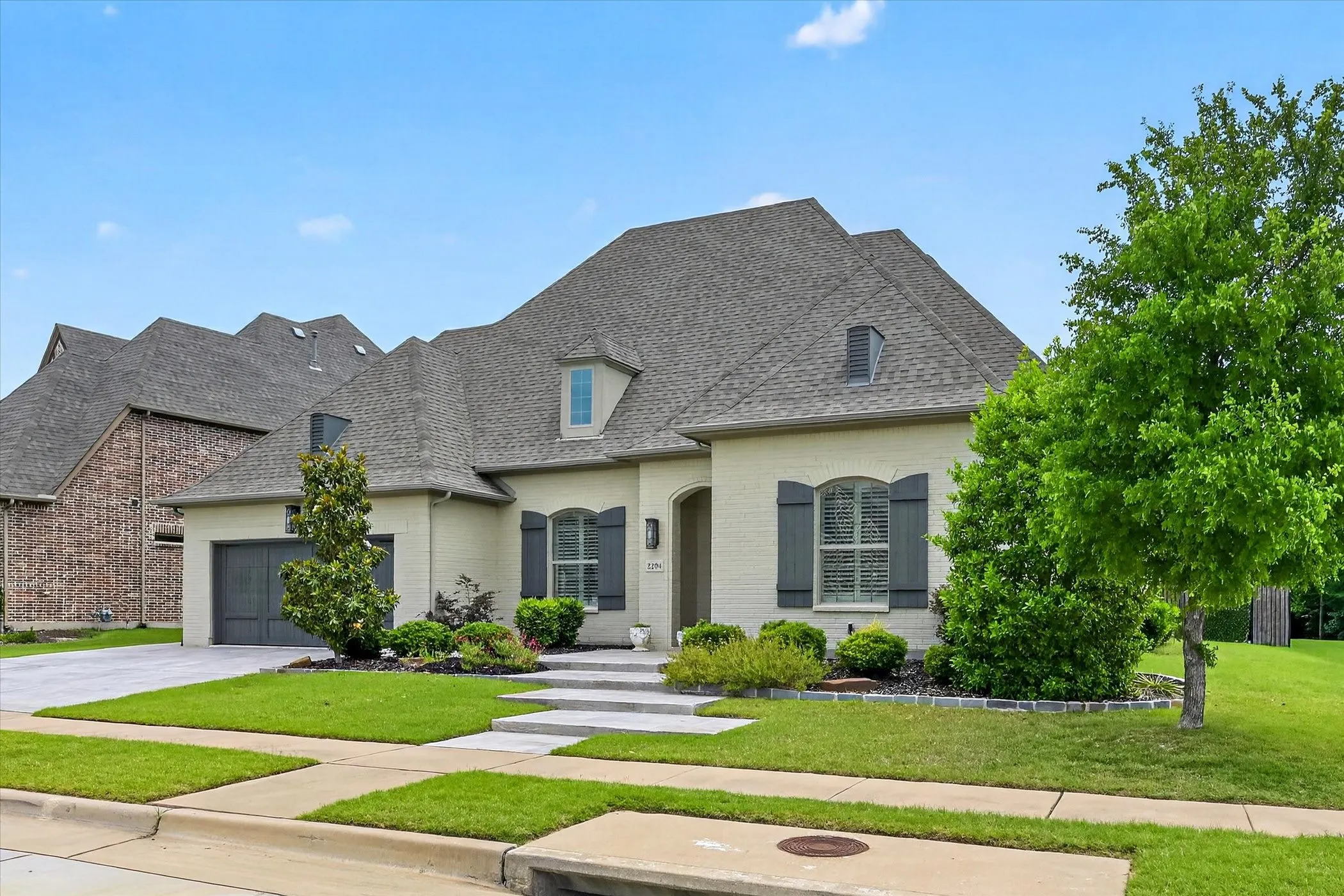 Contemporary single-story residence featuring a light-colored brick exterior, dark grey shutters, and a matching garage door