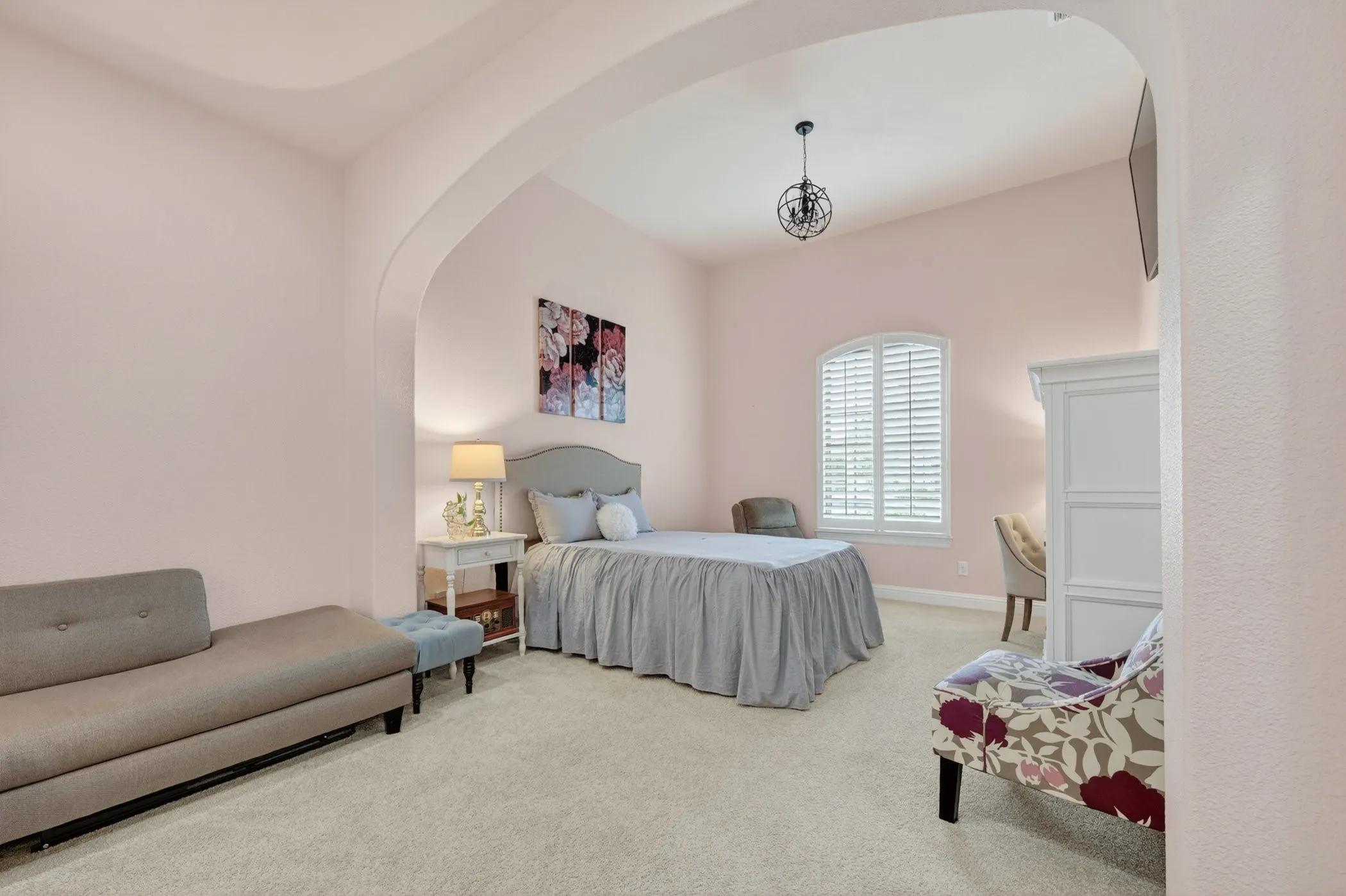 Arched entryway leading to a bedroom featuring an arched window with plantation shutters, a vaulted ceiling, and a spherical wrought iron chandelier
