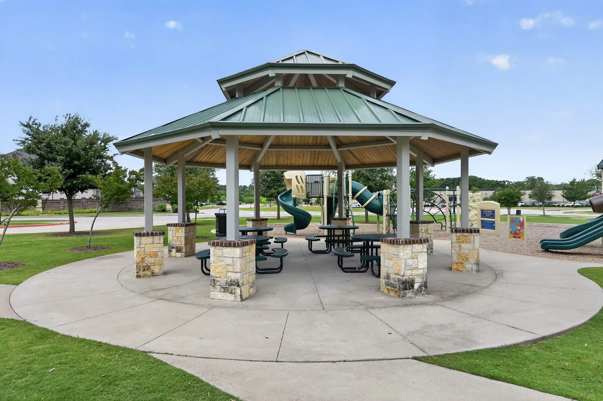Community gazebo featuring a metal roof, stone-clad pillars, and a concrete foundation