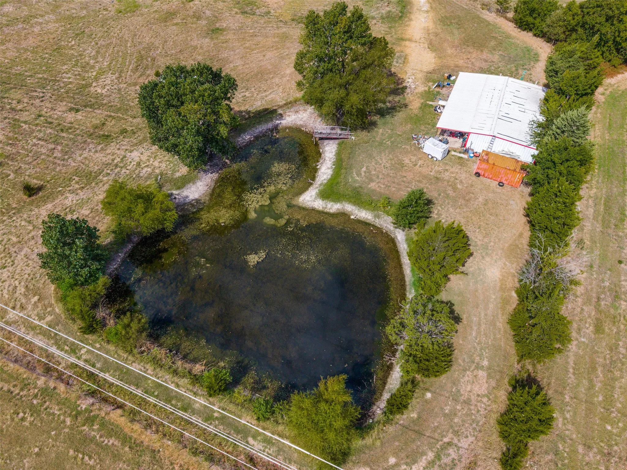 Expansive land featuring a large pond with a footbridge, mature trees, and a metal-roofed outbuilding