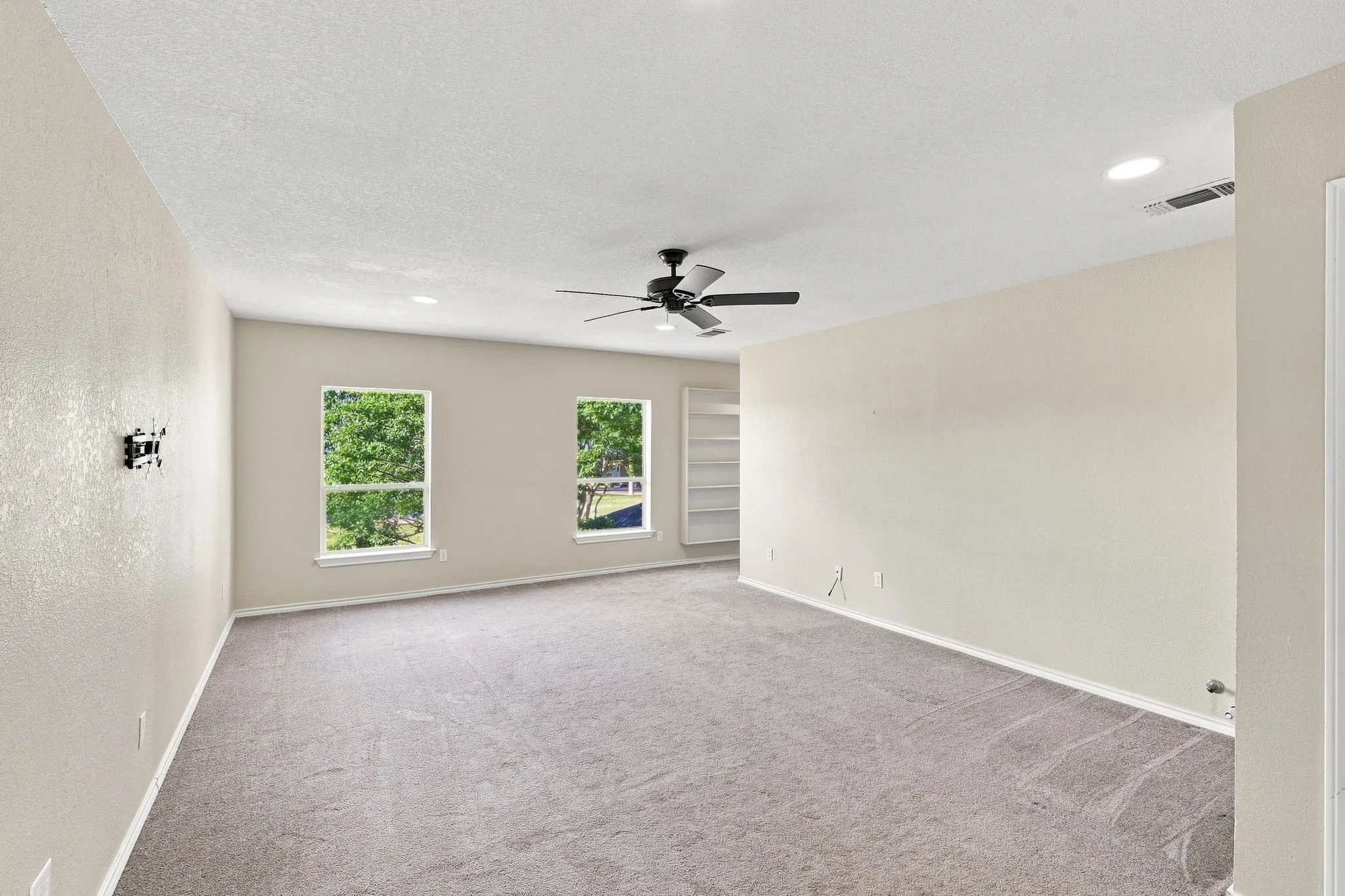 Cozy, light-filled room with recessed lighting, a ceiling fan, two windows, and built-in shelving, flexible space for any lifestyle.