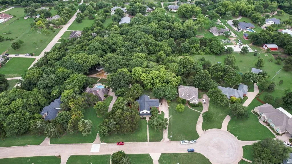 Aerial view highlights the home’s beautiful setting, mature trees, spacious lot, and peaceful neighborhood surroundings