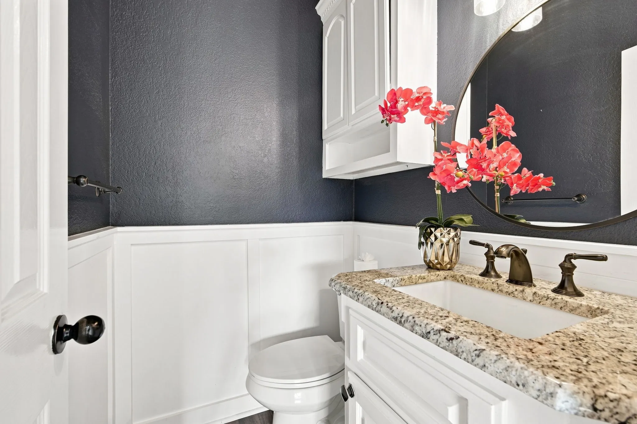 Stylish powder bath accented with white wainscoting and a bold dark wall color.