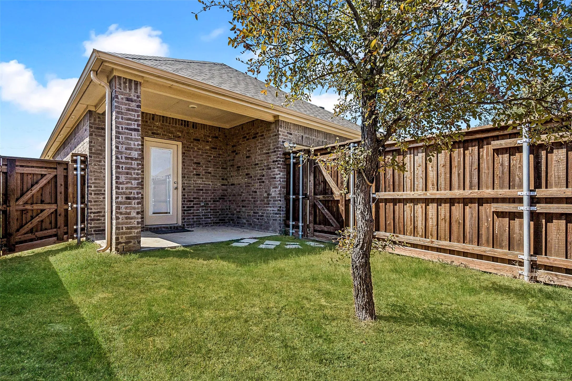 Covered patio with a brick exterior, framed by a wooden privacy fence and a gated entry