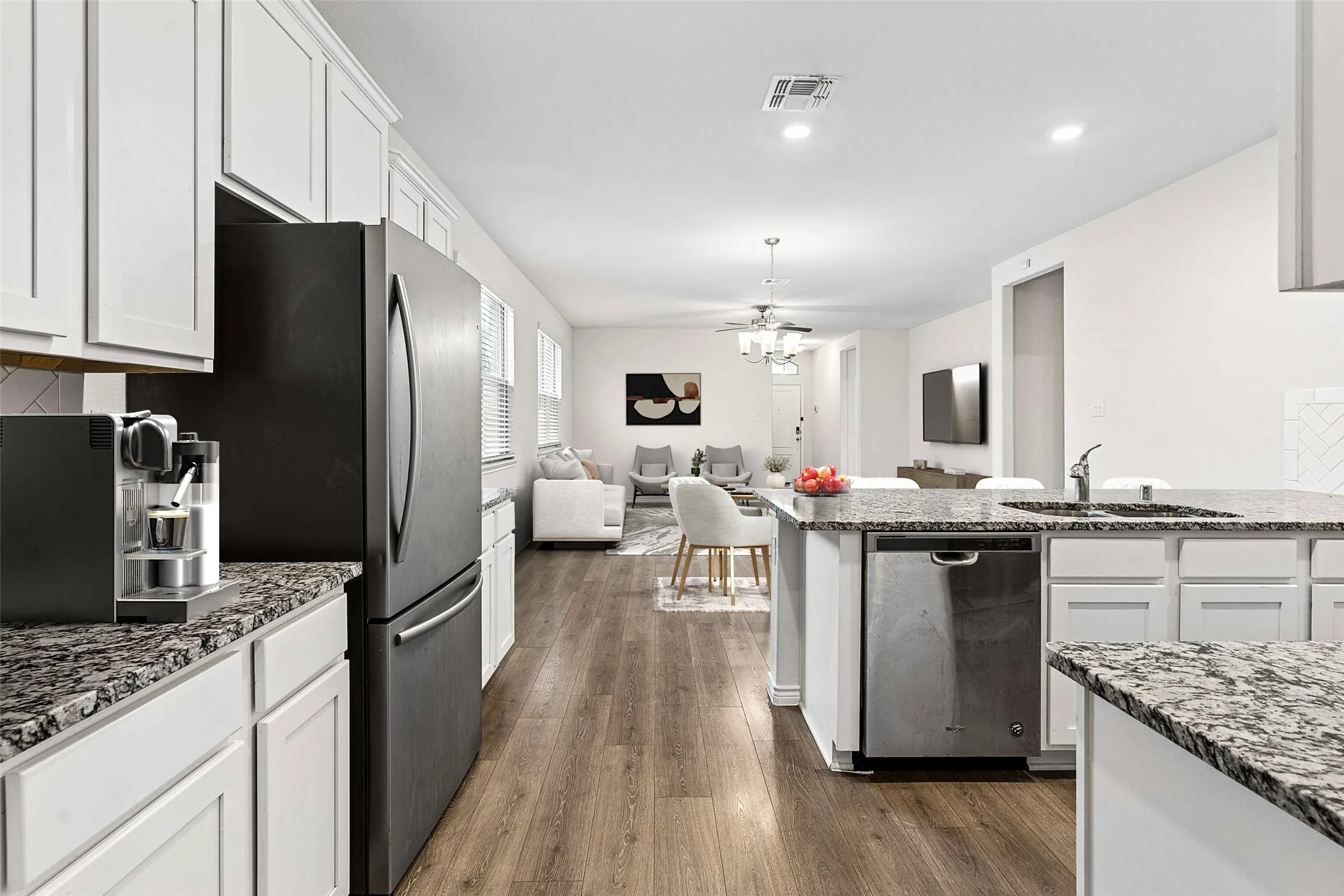 Kitchen featuring white shaker cabinetry, granite countertops, wood-finish flooring, a stainless steel dishwasher, and an integrated sink with a pull-down faucet