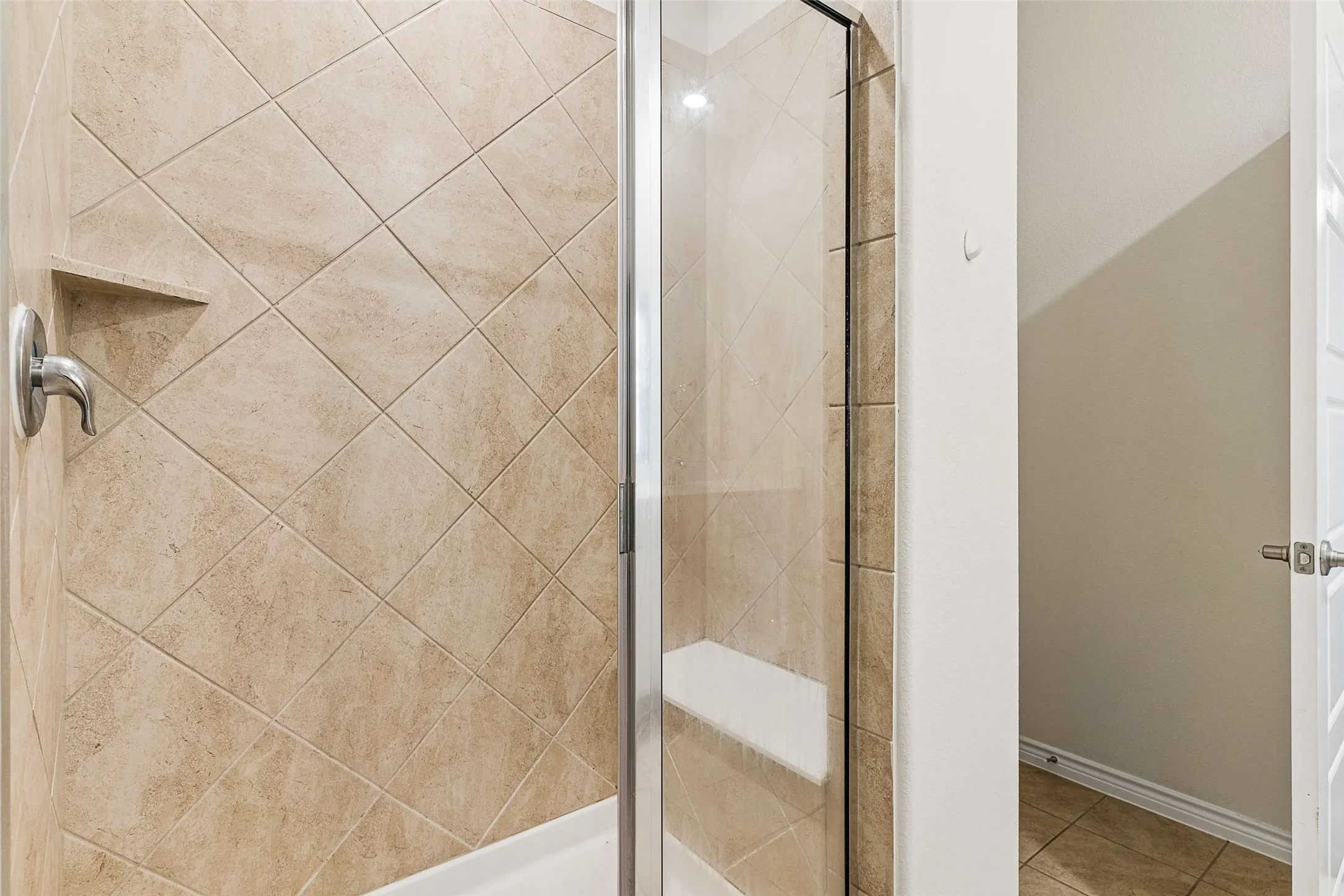 Tiled shower enclosure with diamond-patterned wall tiles, an integrated shower niche, and a built-in shower bench