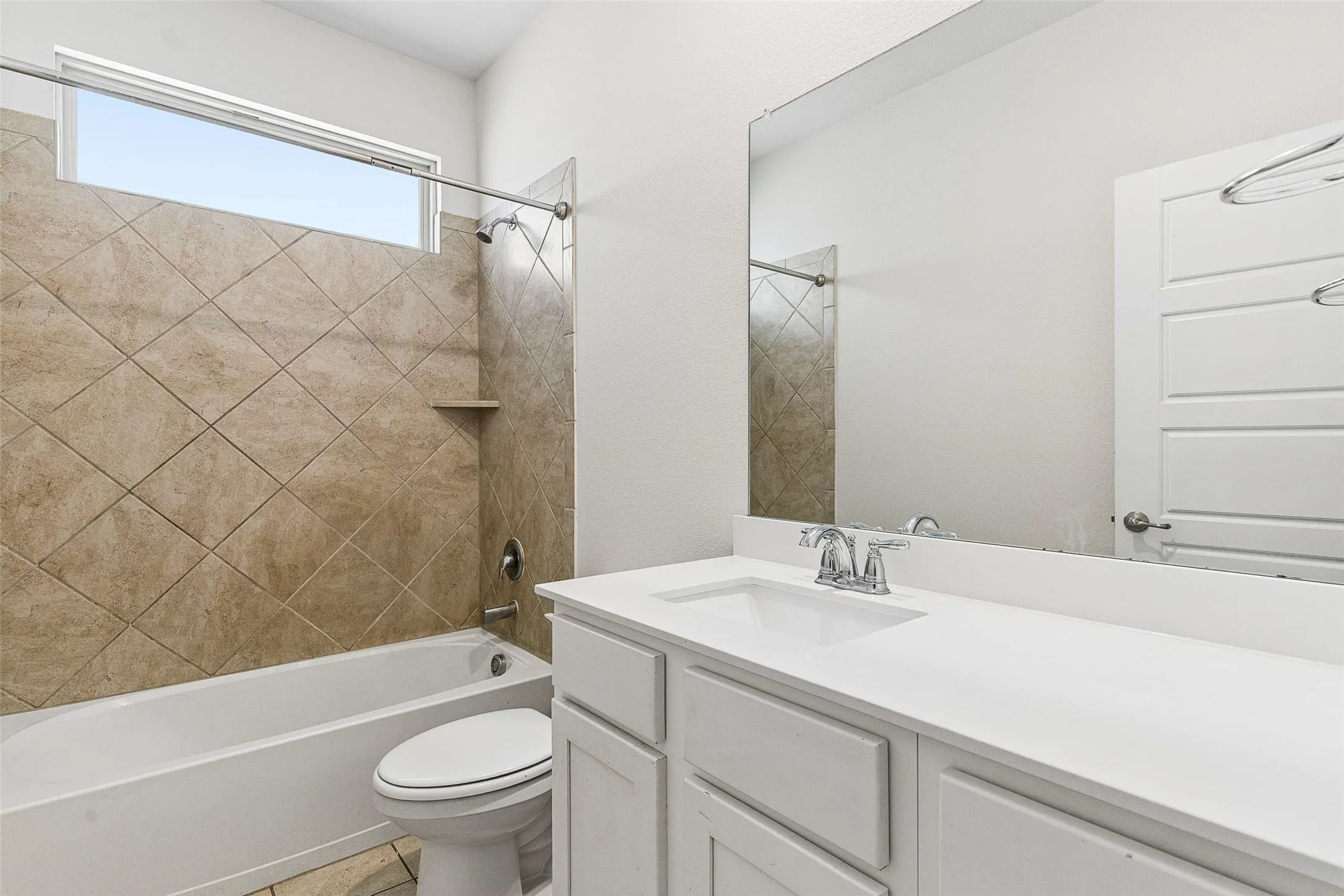 White vanity with an integrated sink and chrome faucet, large mirror, and a combination shower/tub with diagonal tile surround