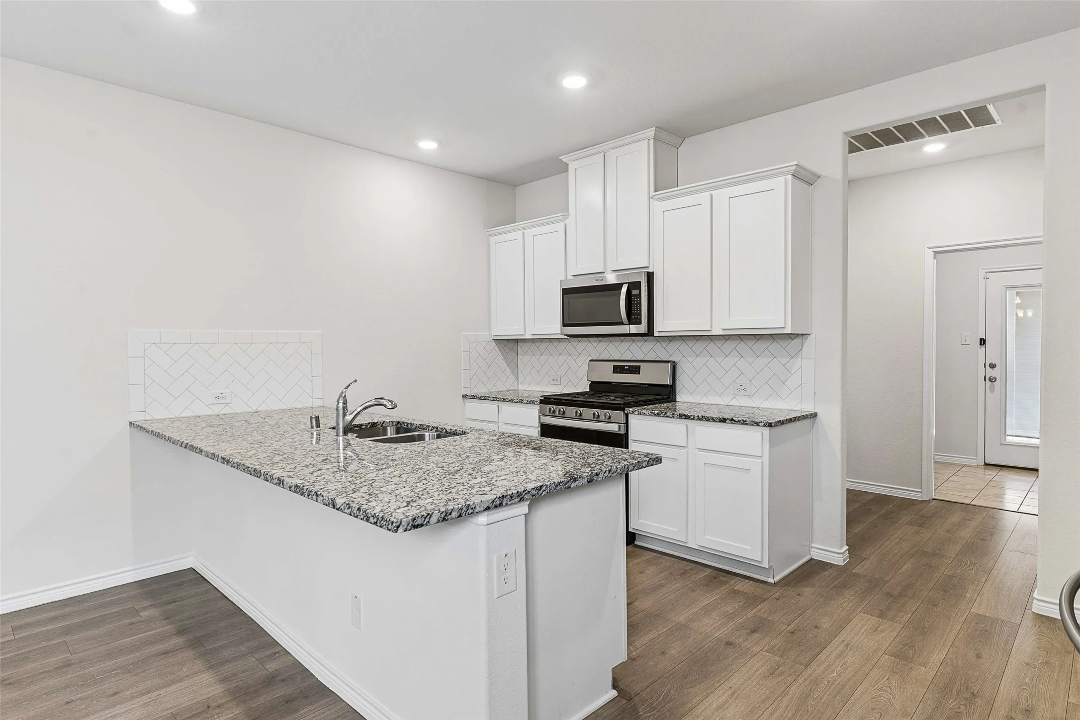 Kitchen featuring white cabinetry, granite countertops, stainless steel appliances, a white subway tile backsplash, and wood-finish flooring