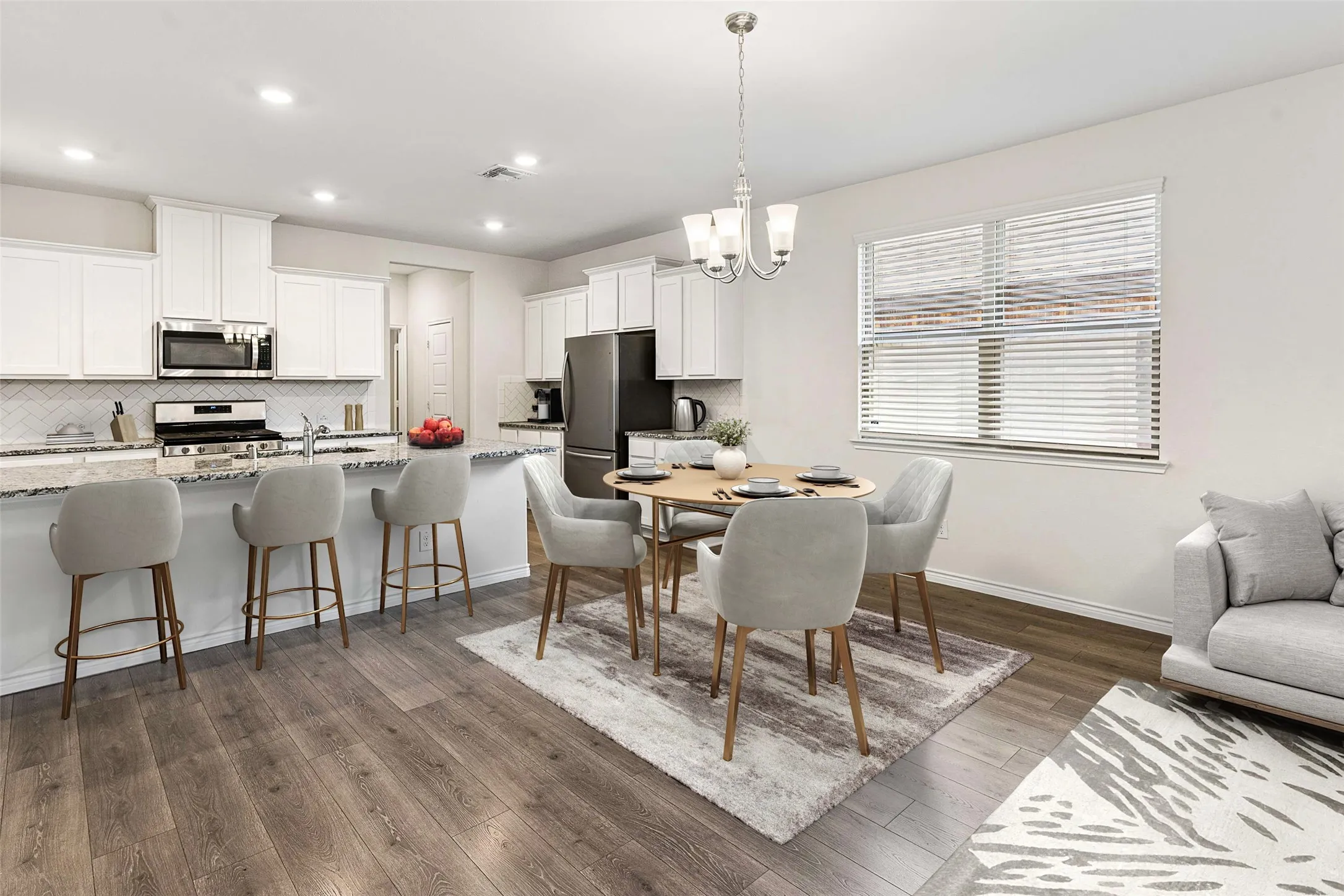 Integrated kitchen and dining area featuring wood-finish flooring, white cabinetry, a kitchen island with seating, stainless steel appliances, and a window with blinds
