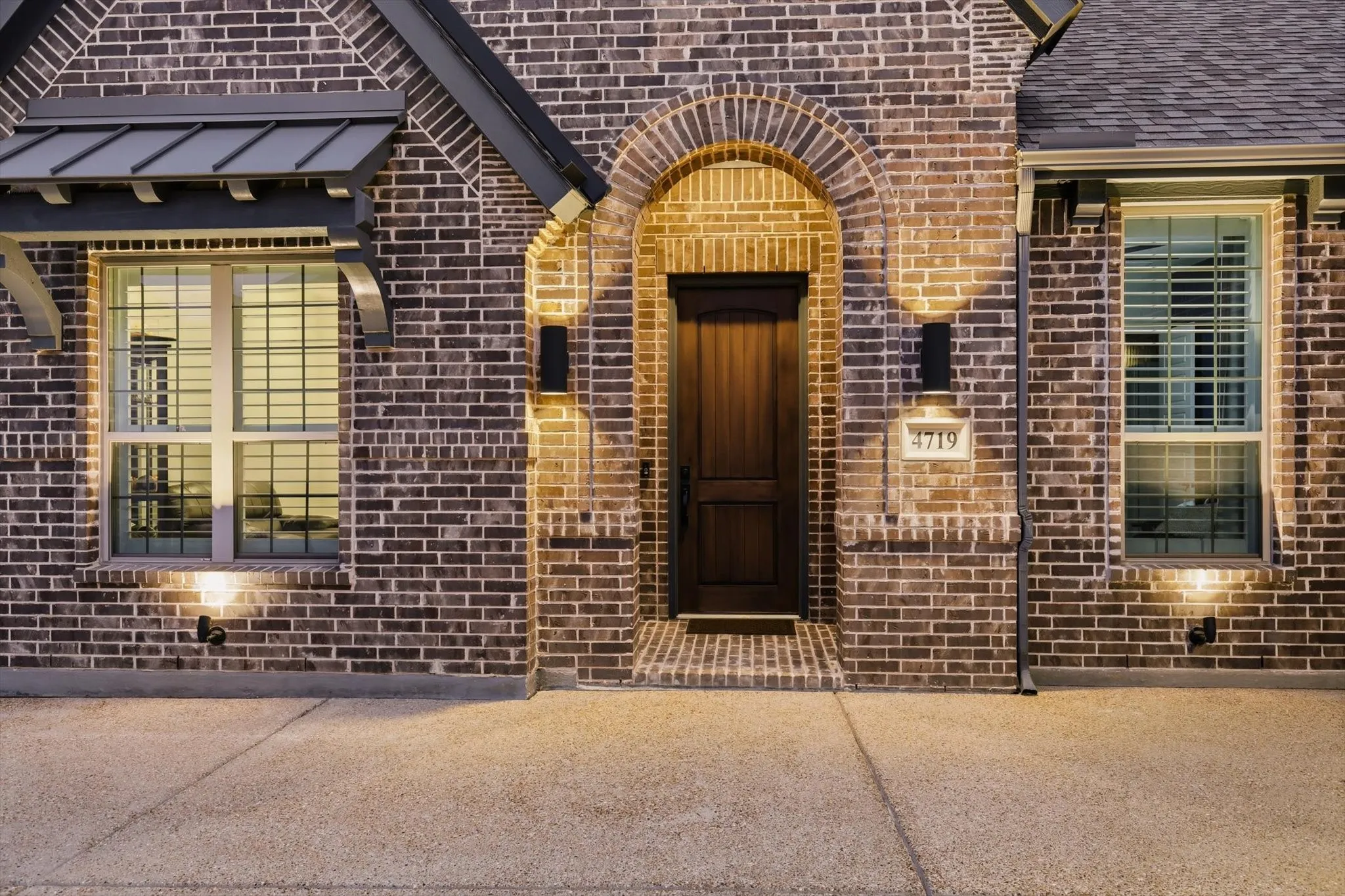 Brick exterior with stone accents, arched entryway, wood-finish front door, and decorative window awnings