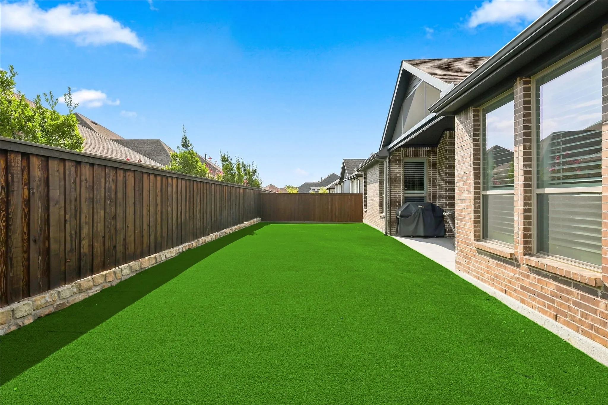 Expansive green lawn with a stone and wood privacy fence, brick exterior, and covered patio