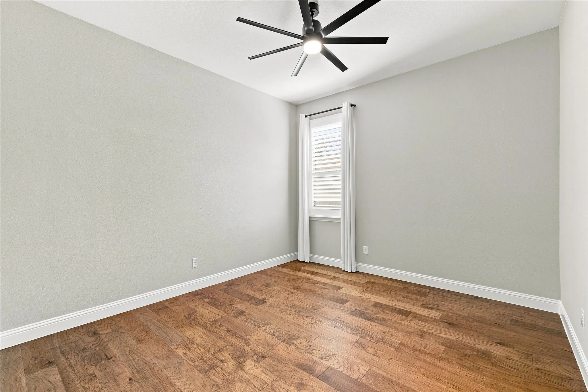 Wood-finish flooring with white trim, a window with horizontal blinds, and a ceiling fan with integrated lighting