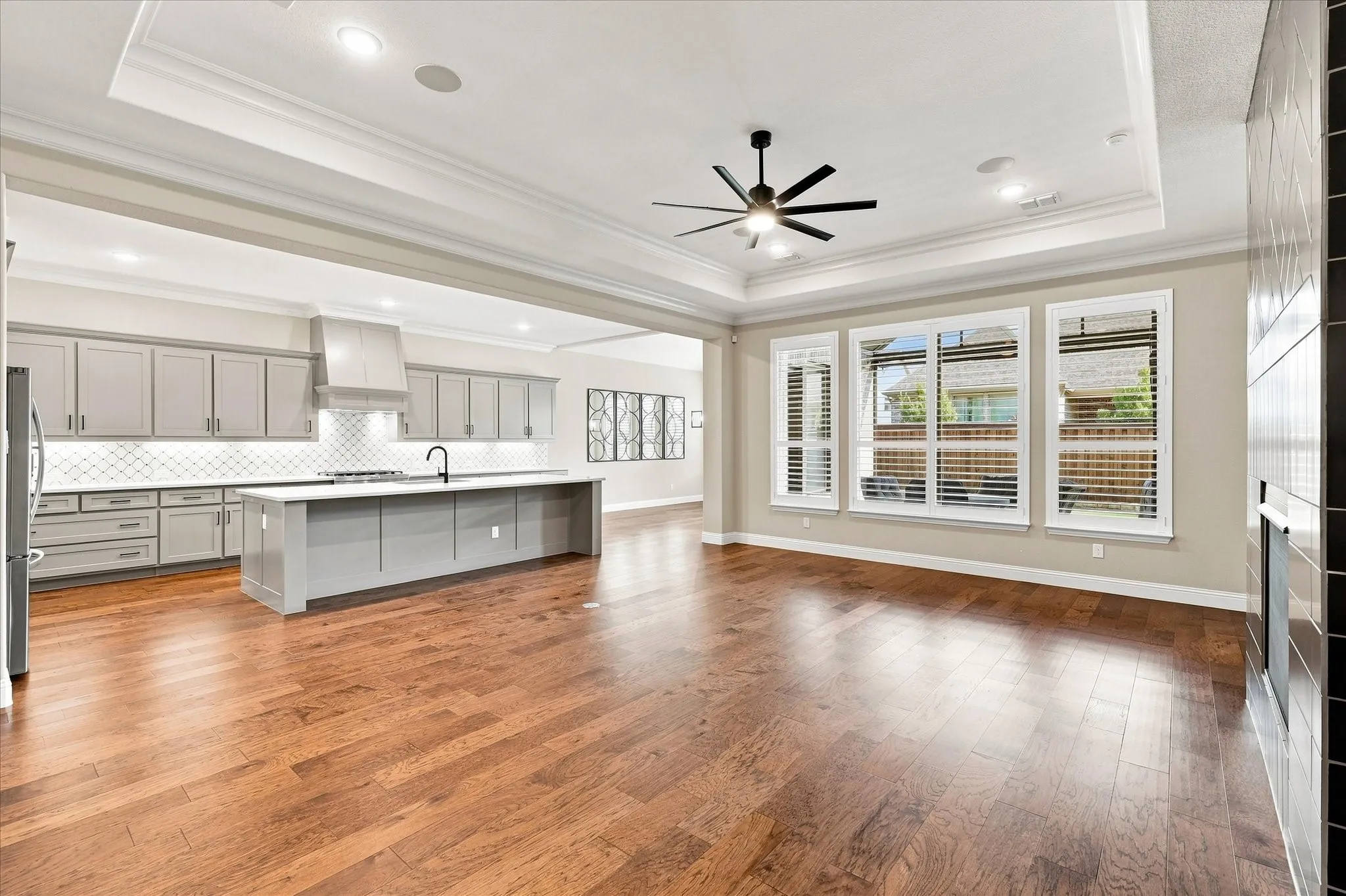 Hardwood-finish flooring throughout, tray ceiling with recessed lighting, black ceiling fan, and multiple large windows with horizontal blinds