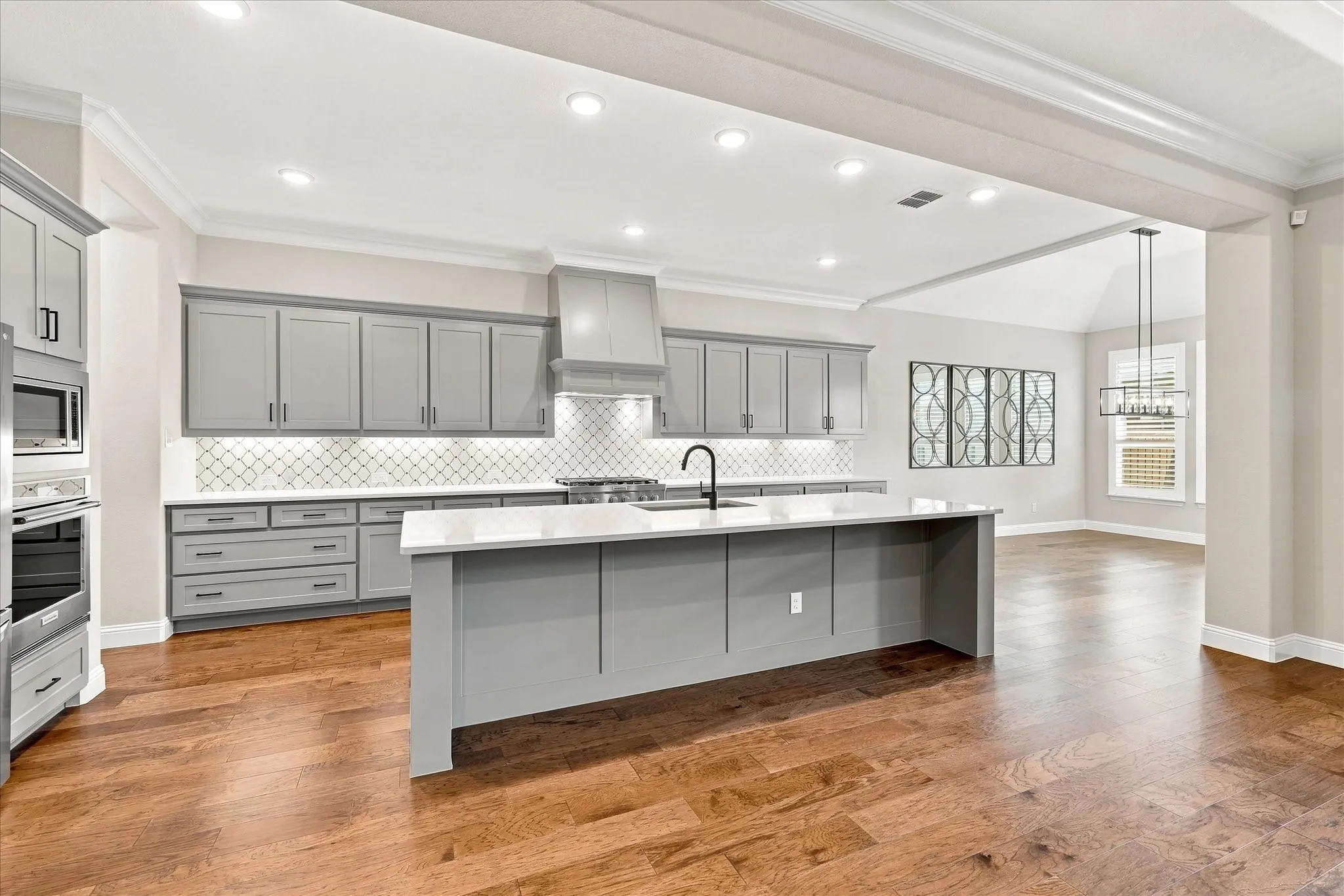 Kitchen featuring wood-finish flooring, gray cabinetry, a central island with a white countertop, stainless steel appliances, and a tile backsplash