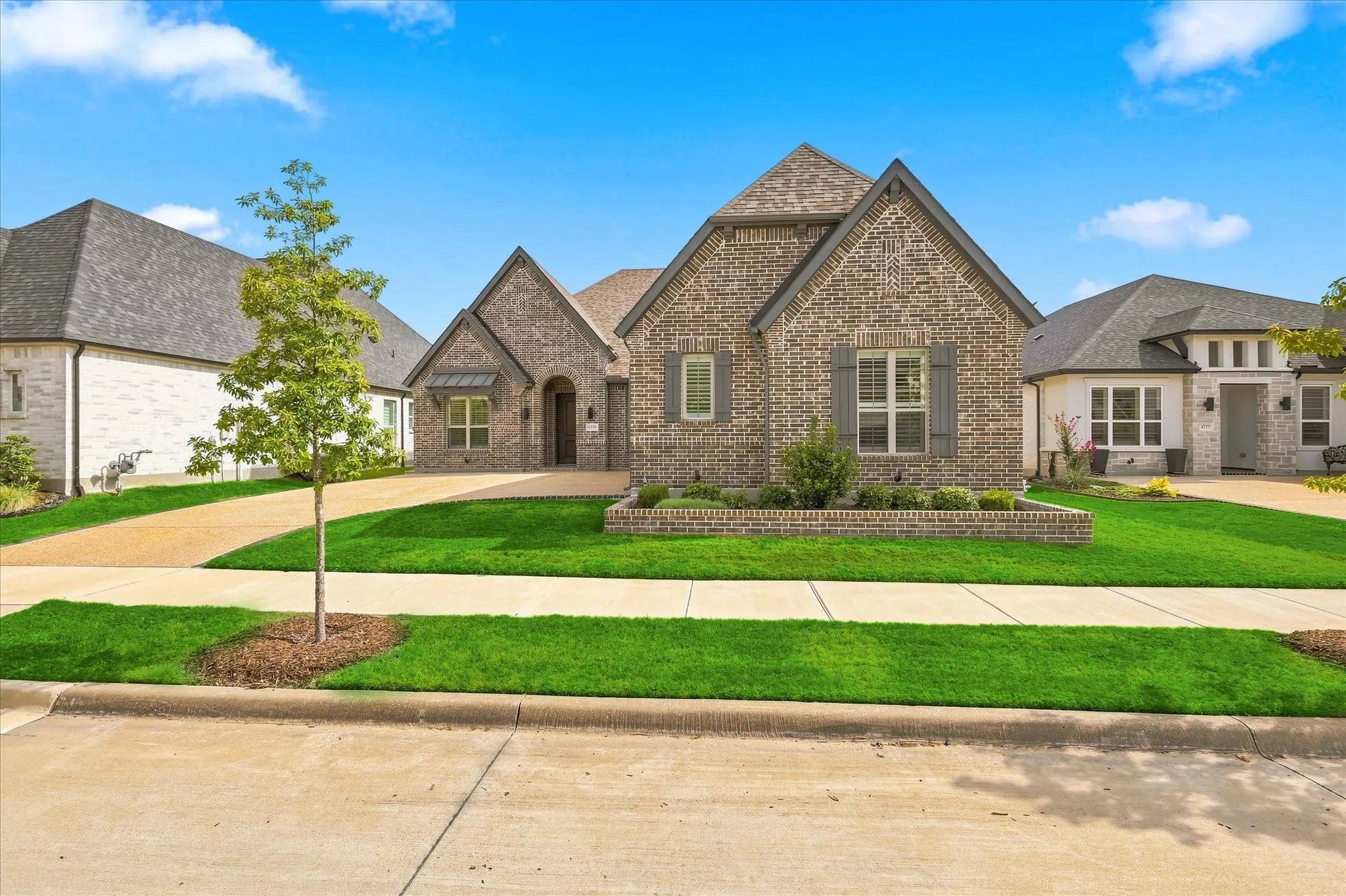 Brick facade with gabled roof lines, featuring gray window shutters, an arched entry, and a brick-lined flower bed