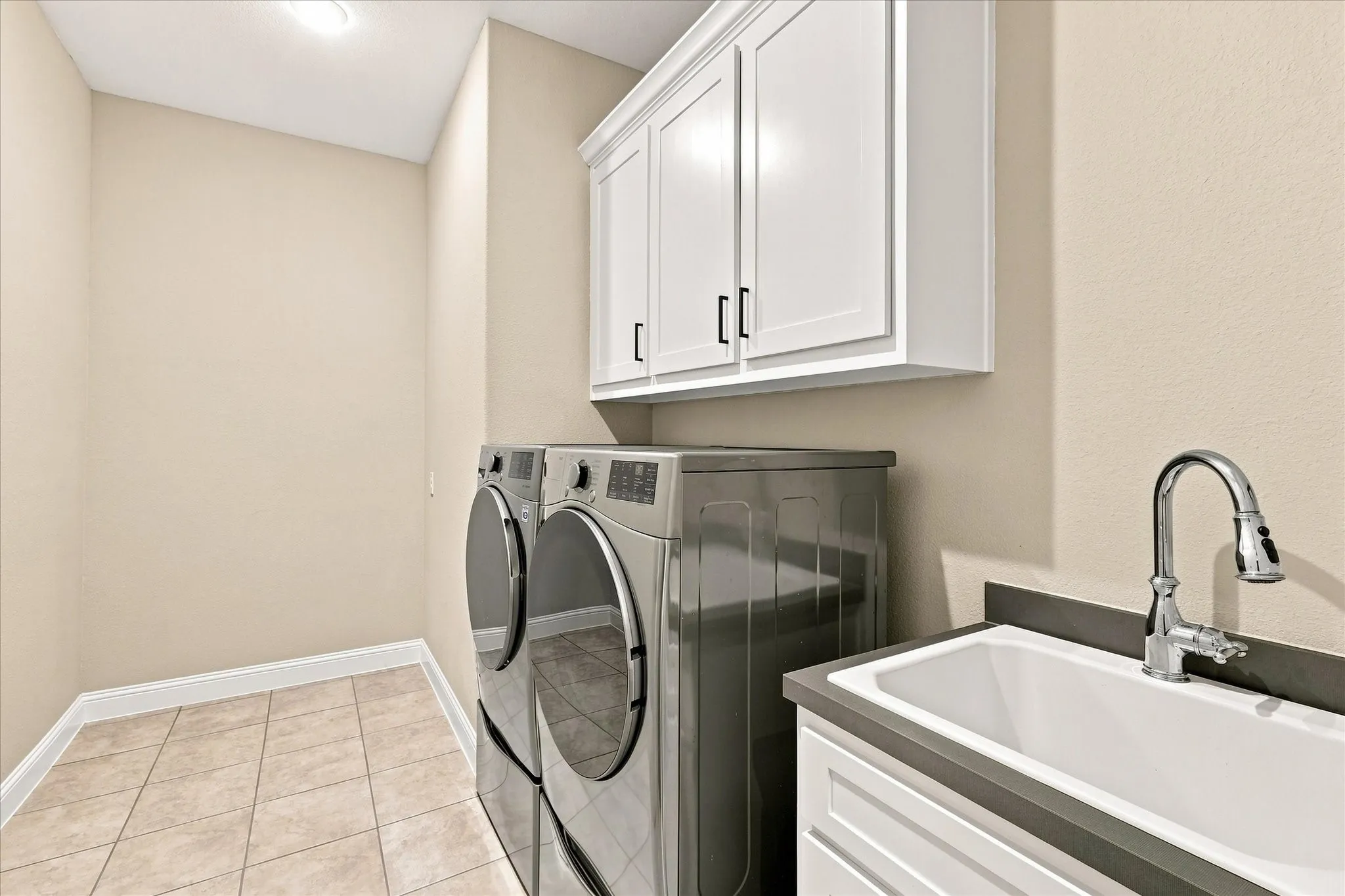 Laundry area featuring neutral wall tones, tiled flooring, white cabinetry with black hardware, a utility sink with a chrome faucet, and recessed lighting