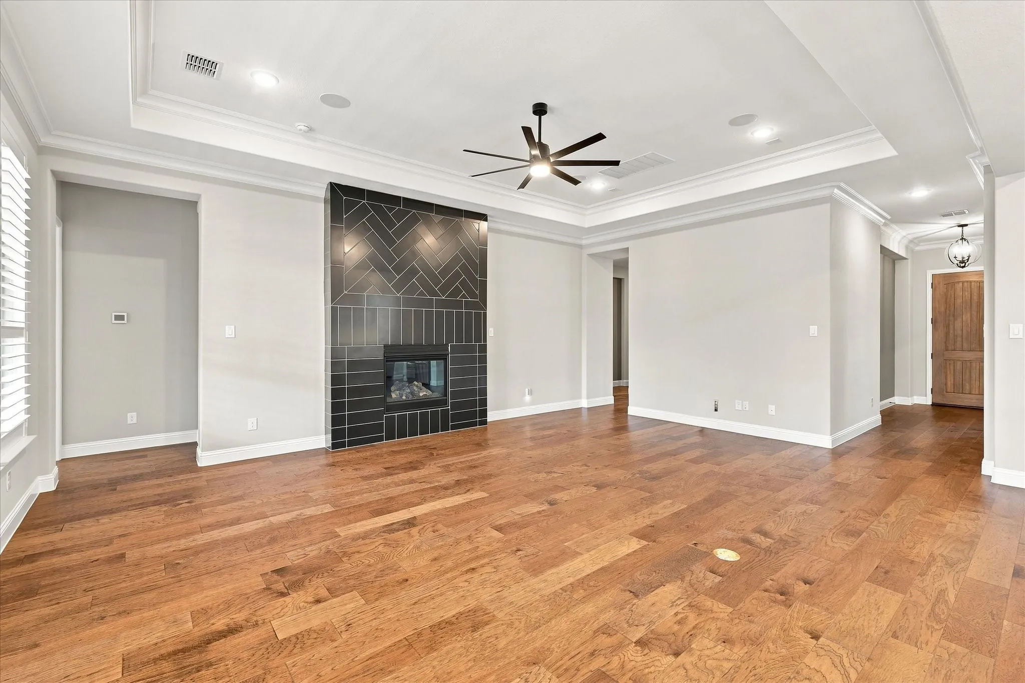 Hardwood flooring, tray ceiling, recessed lighting, contemporary fireplace with herringbone tile surround, and a ceiling fan