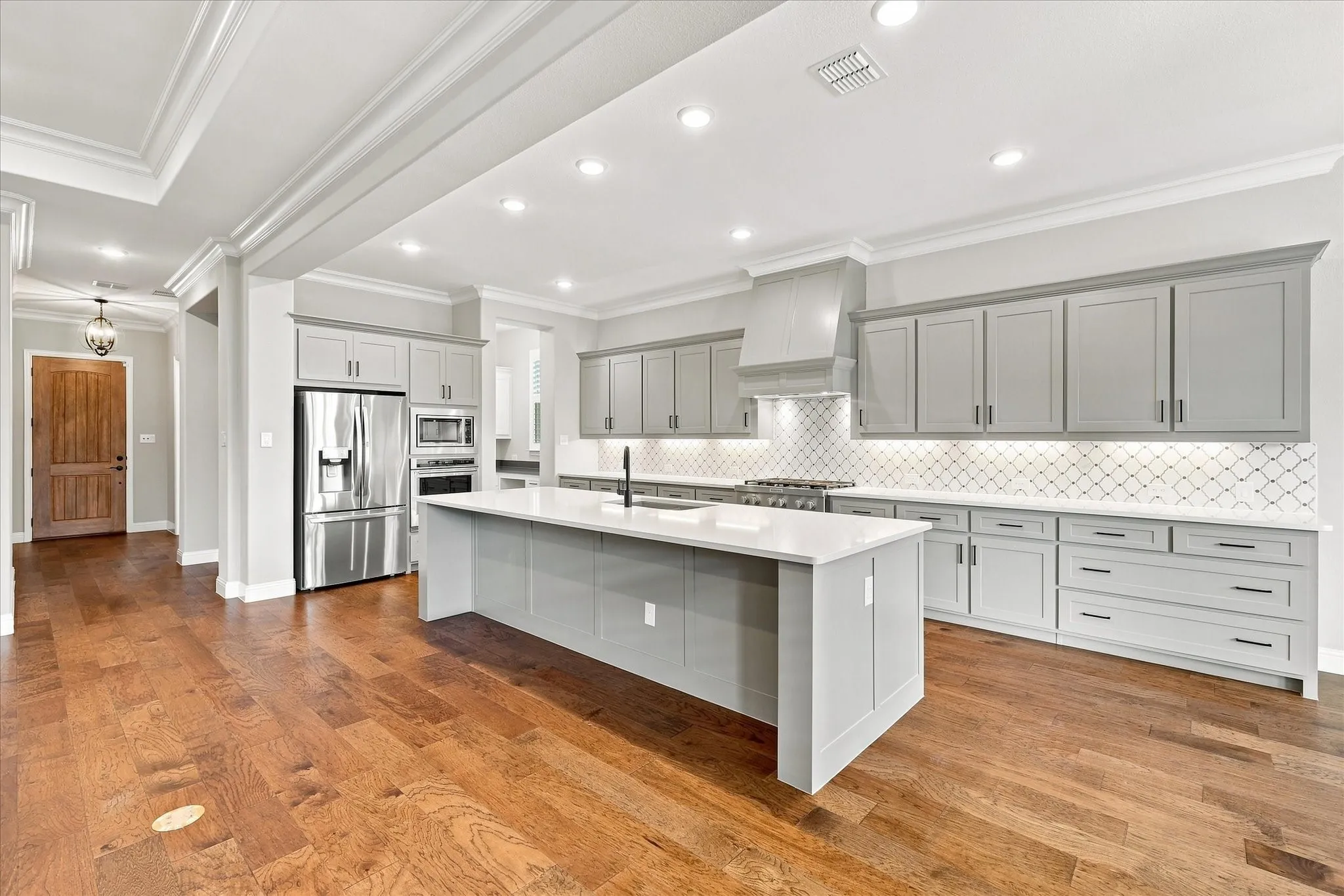Spacious kitchen featuring an expansive center island, light gray cabinetry, stainless steel appliances, and wood-finish flooring