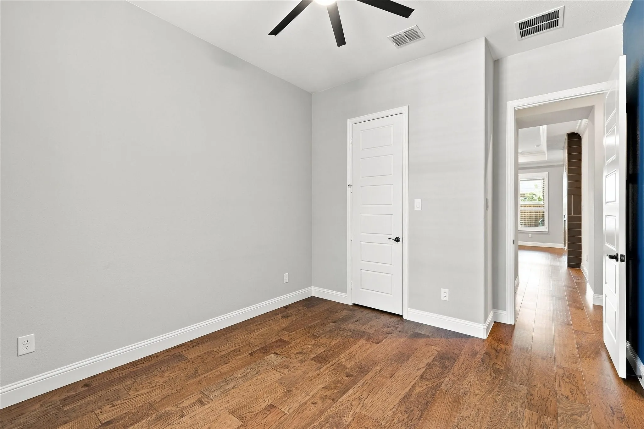 Wood-finish flooring throughout, white trim, white paneled doors, and a ceiling fan