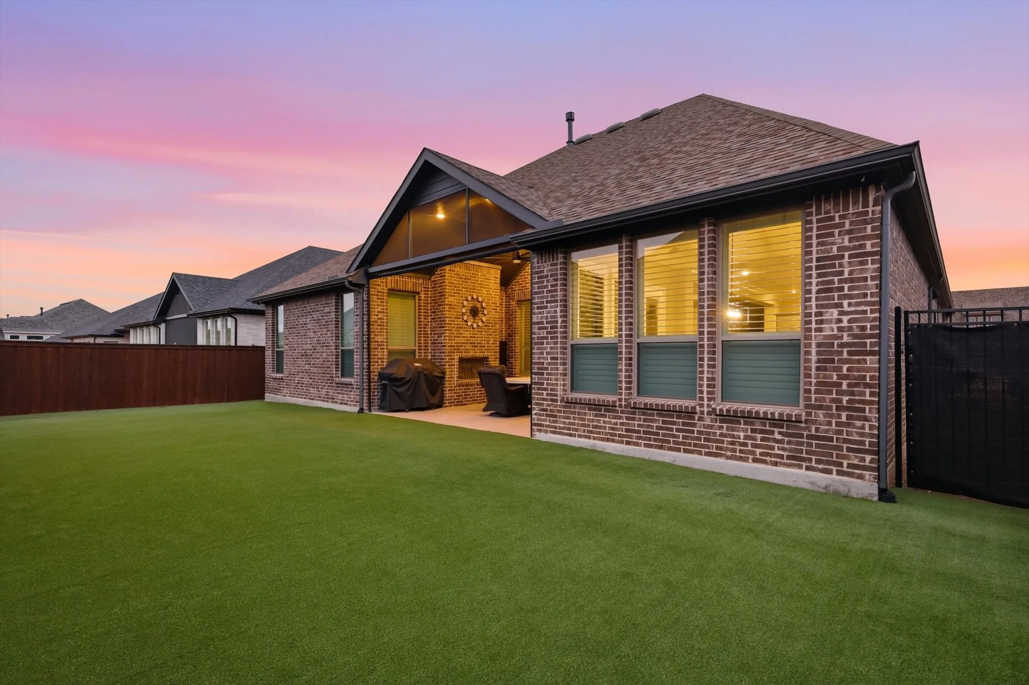 Brick exterior with multiple windows, covered patio, built-in outdoor fireplace, and expansive green lawn