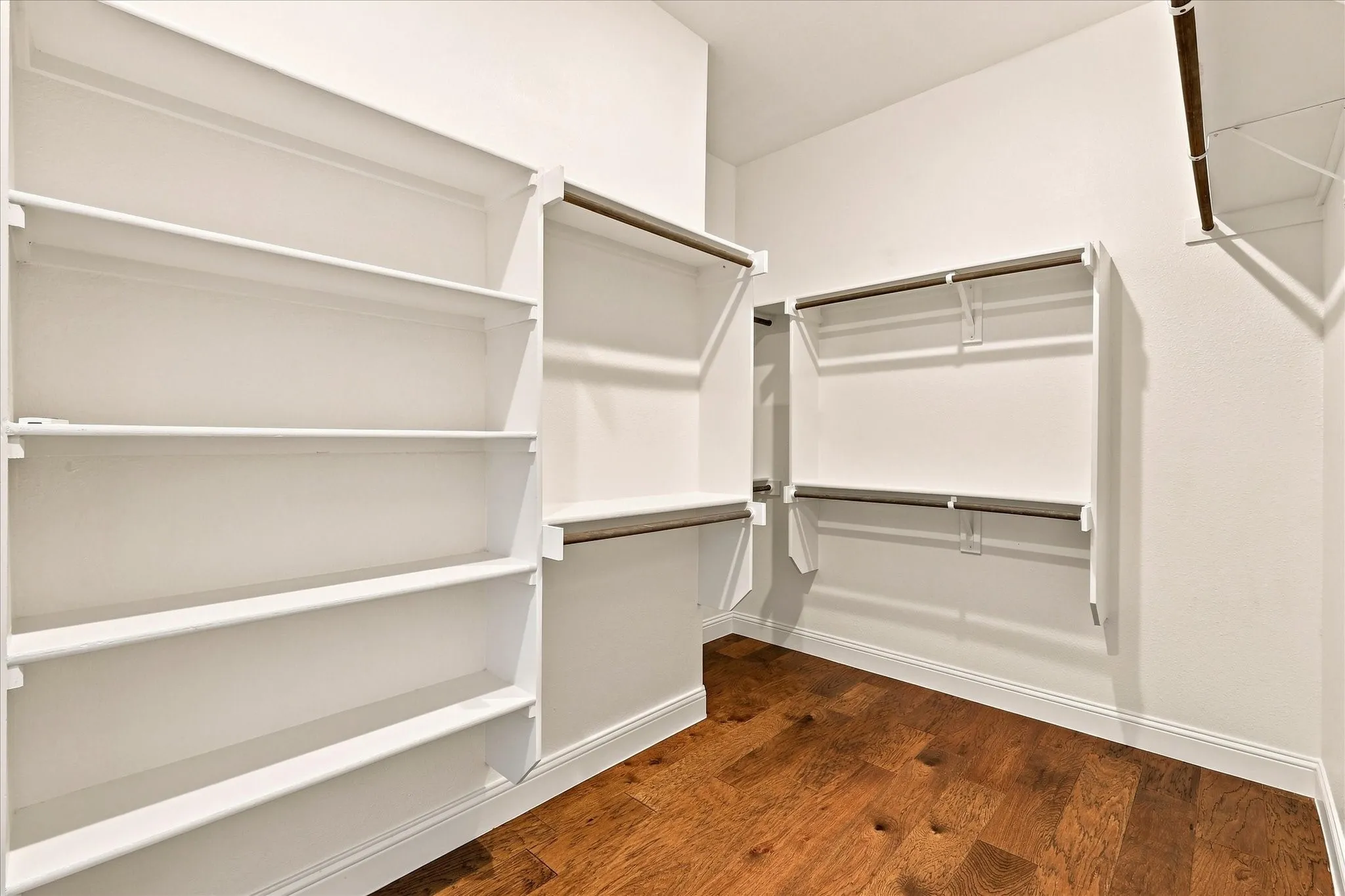 White built-in shelving, multiple hanging rods, and wood-finish flooring
