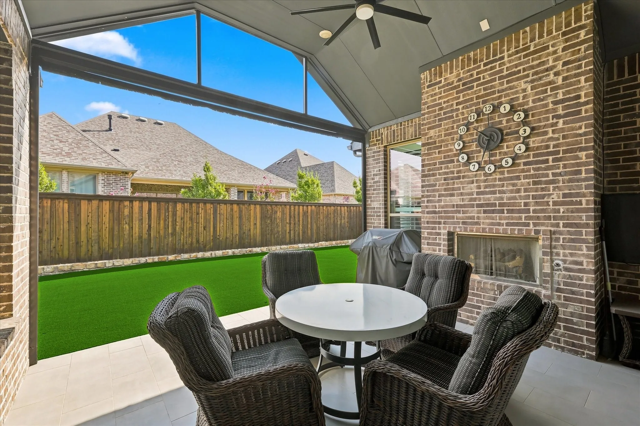 Covered outdoor patio featuring a brick fireplace, ceiling fan, vaulted roof, and tile flooring