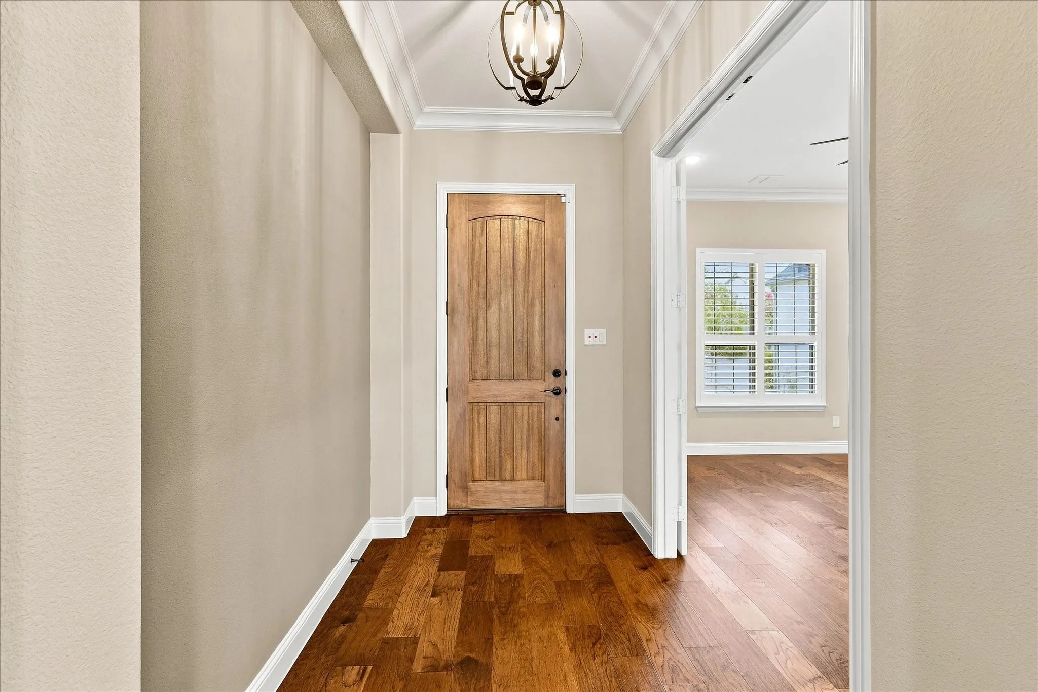 Hardwood flooring throughout, crown molding, paneled wooden entry door, and a decorative ceiling light fixture