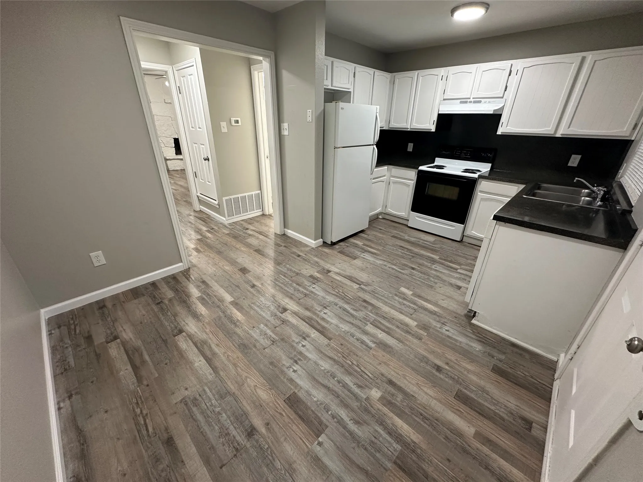 Kitchen featuring wood-finish flooring, white cabinetry, dark countertops, and white appliances