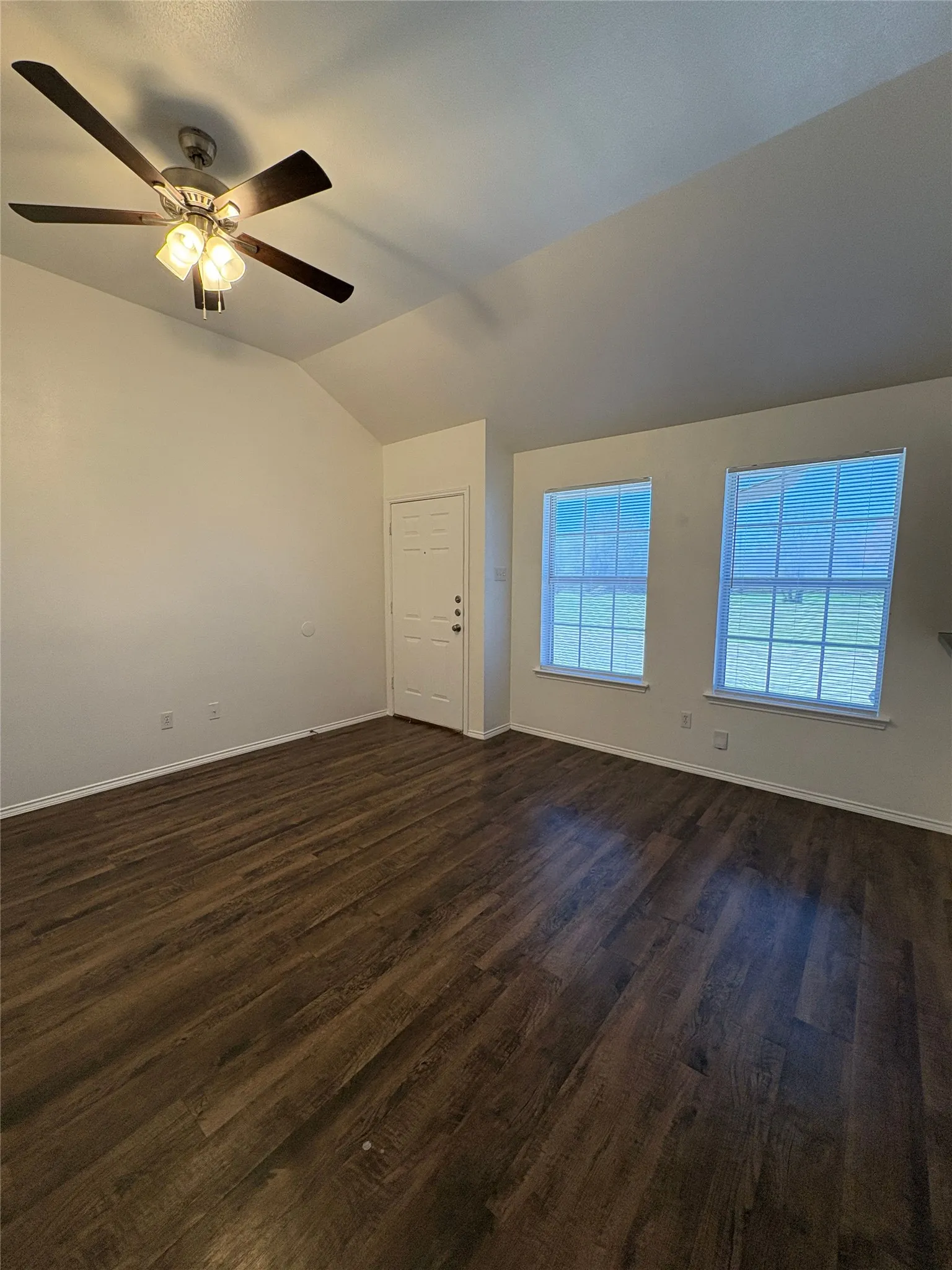 Vaulted ceiling with a ceiling fan light fixture, wood-finish flooring, and two windows with blinds
