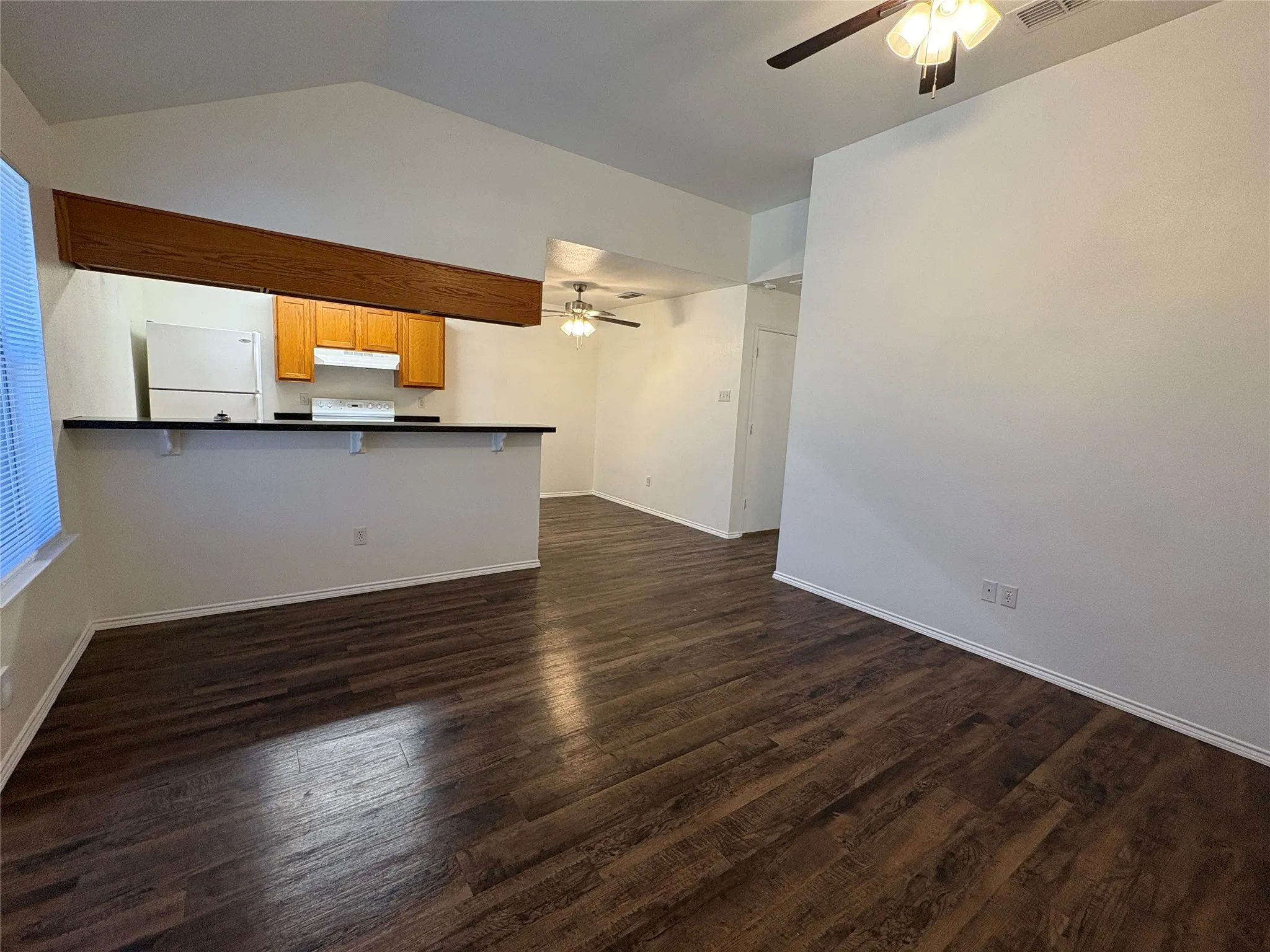 Vaulted ceilings, wood-finish flooring, kitchen with wood cabinetry, breakfast bar, and ceiling fan