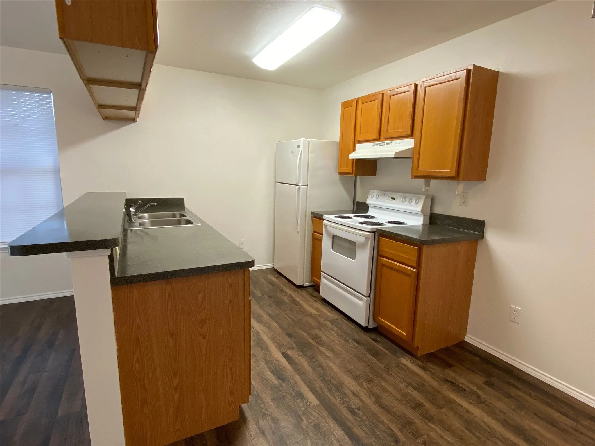 Kitchen featuring wood-finish cabinetry, dark countertops, white appliances, and wood-finish flooring