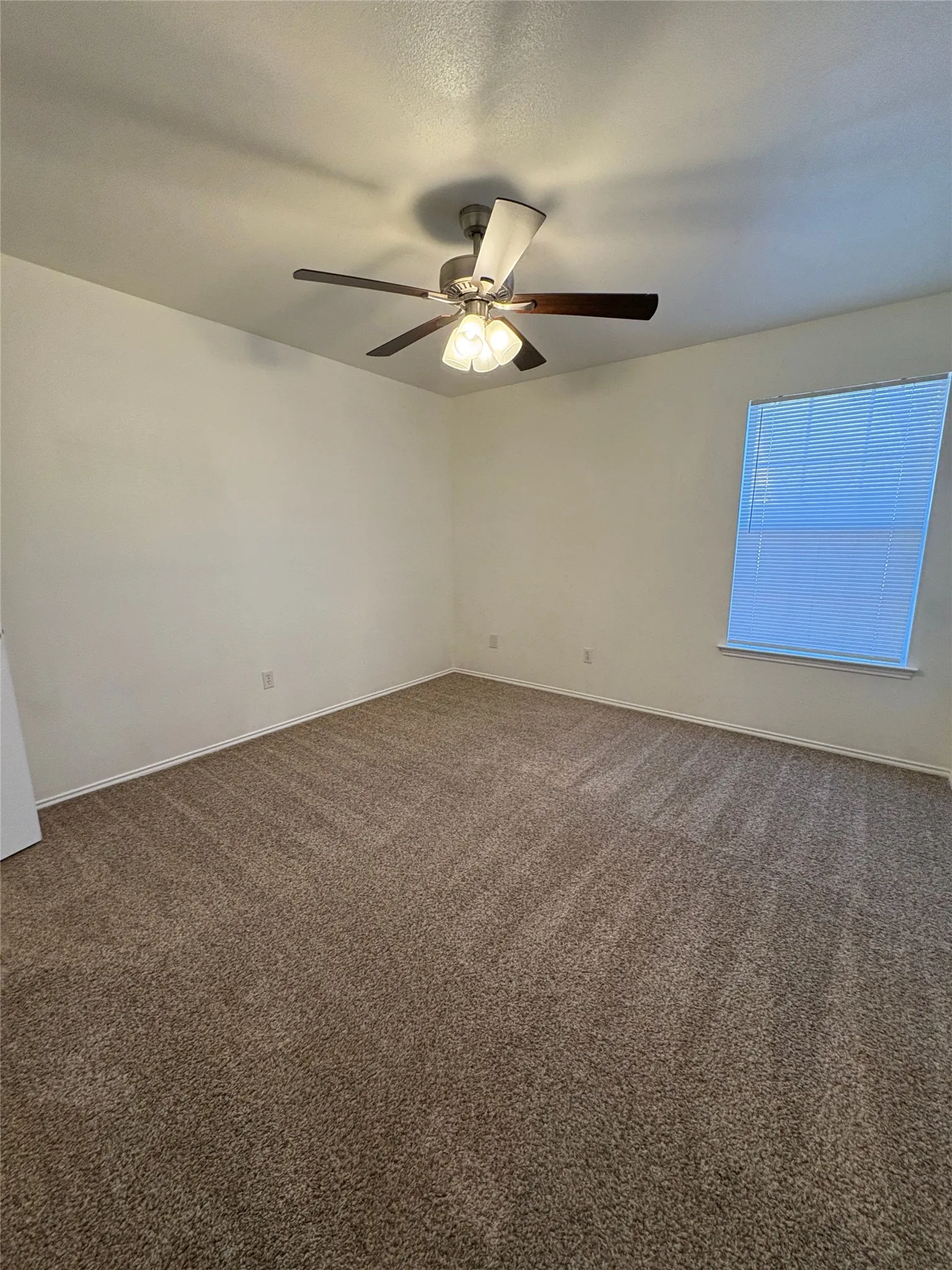 Spacious room with neutral carpeting, overhead ceiling fan with lighting, and a window with horizontal blinds