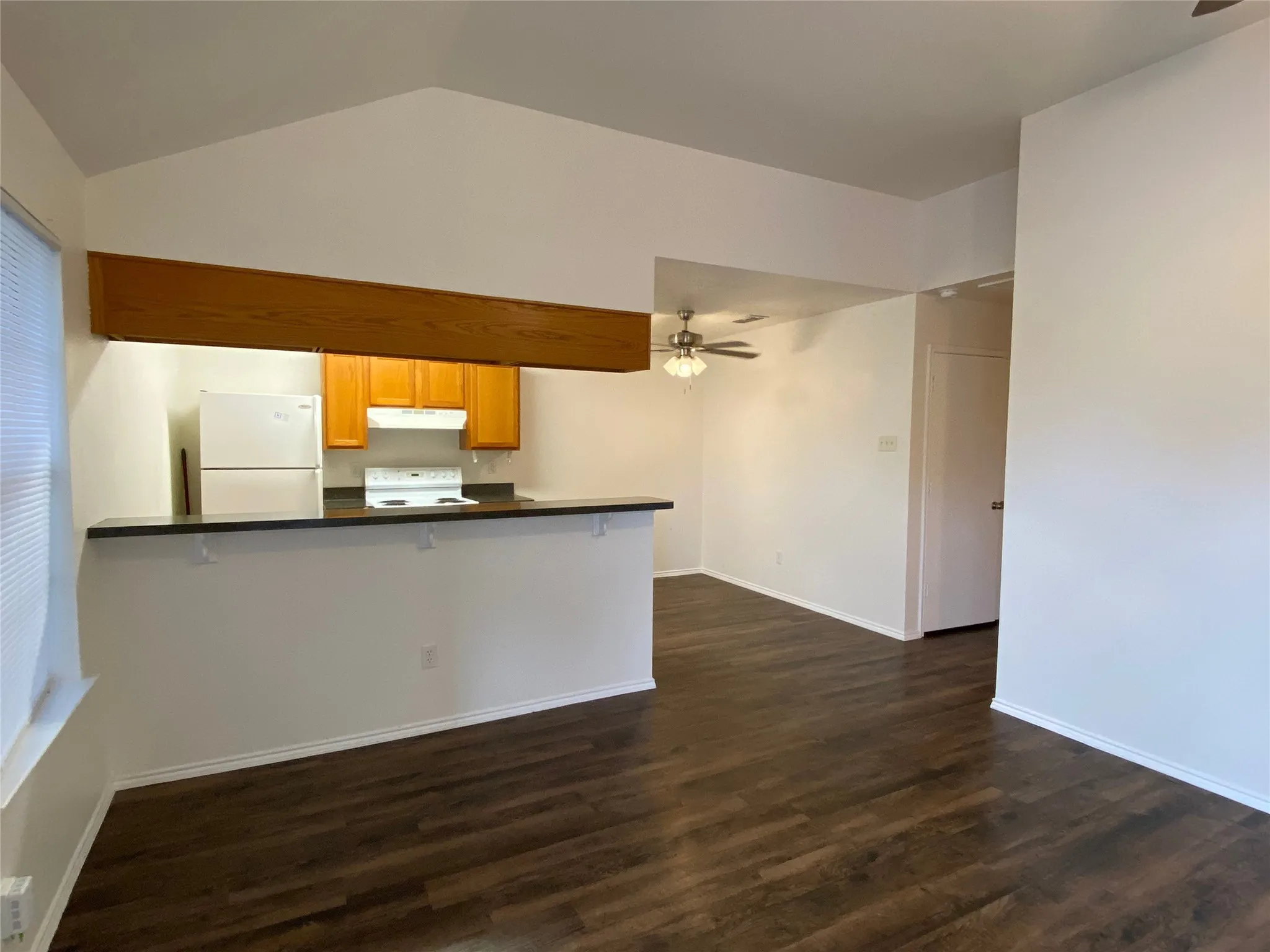 Vaulted ceiling, wood-finish flooring, kitchen with wood cabinetry, and a ceiling fan