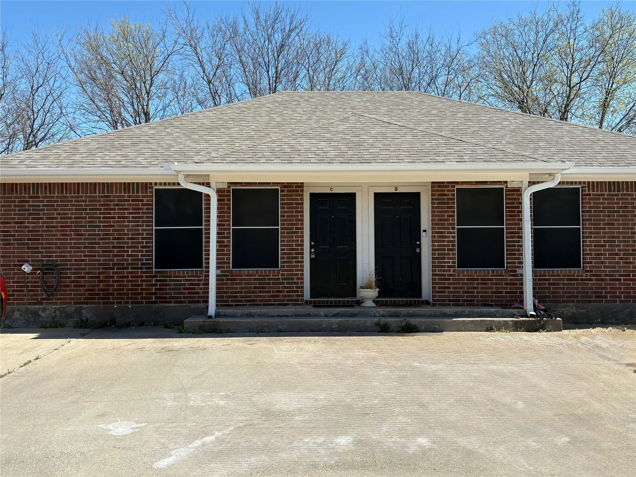 Brick exterior featuring a gabled roof with asphalt shingles, white gutters, and two black entry doors