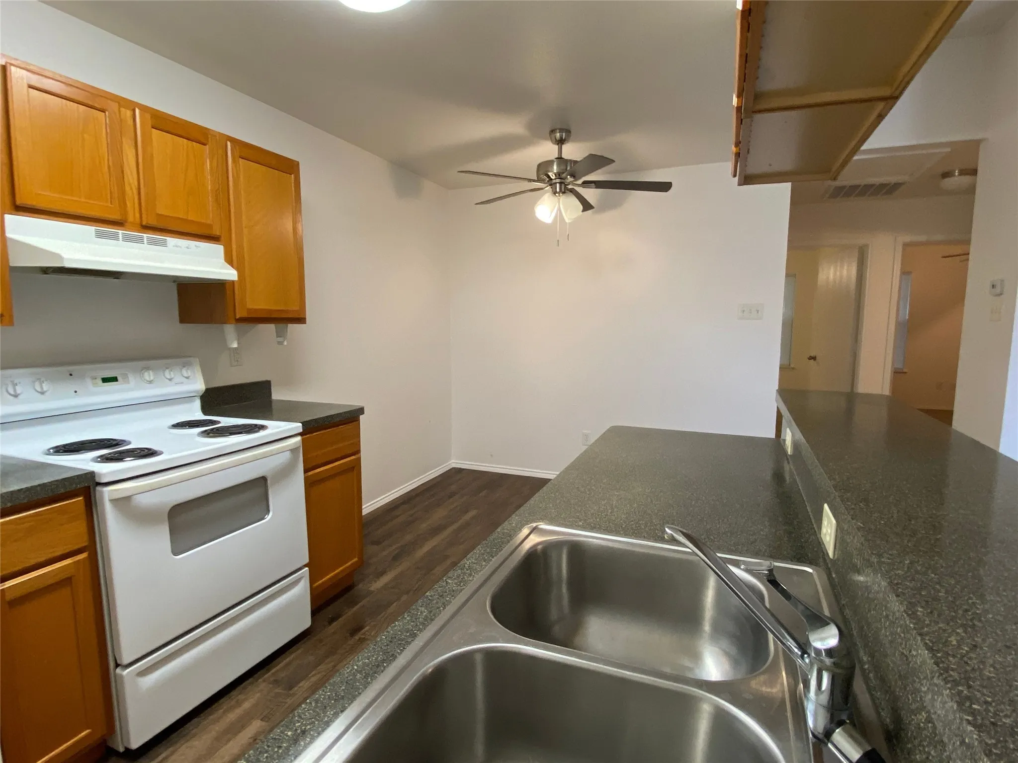 Kitchen featuring wood-finish cabinetry, dark countertops, a double basin sink, and a built-in range