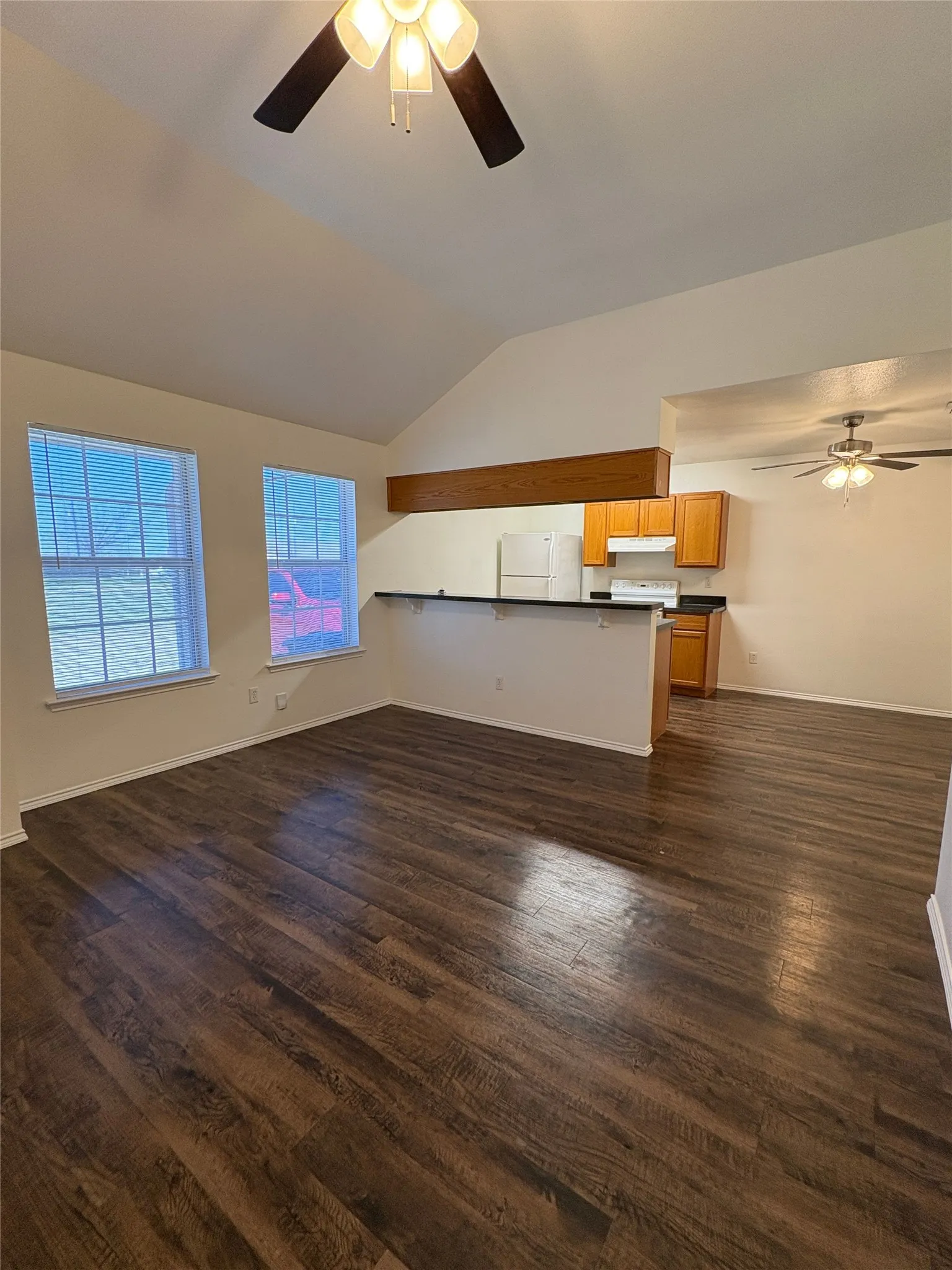 Vaulted ceiling with an exposed beam, wood-finish flooring, and dual windows with blinds