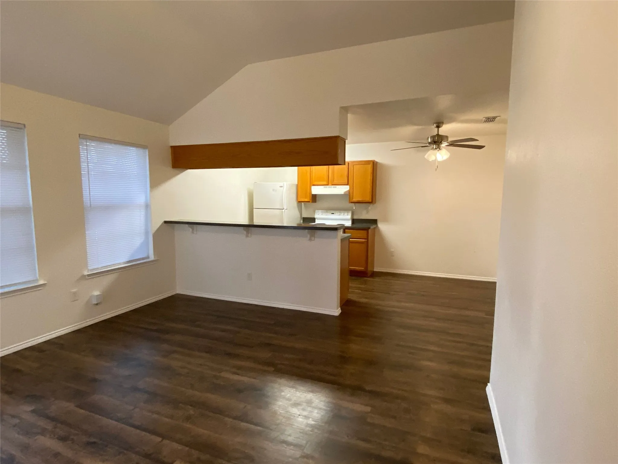 Vaulted ceilings, wood-finish flooring, two windows with blinds, a breakfast bar, and a ceiling fan with light fixture