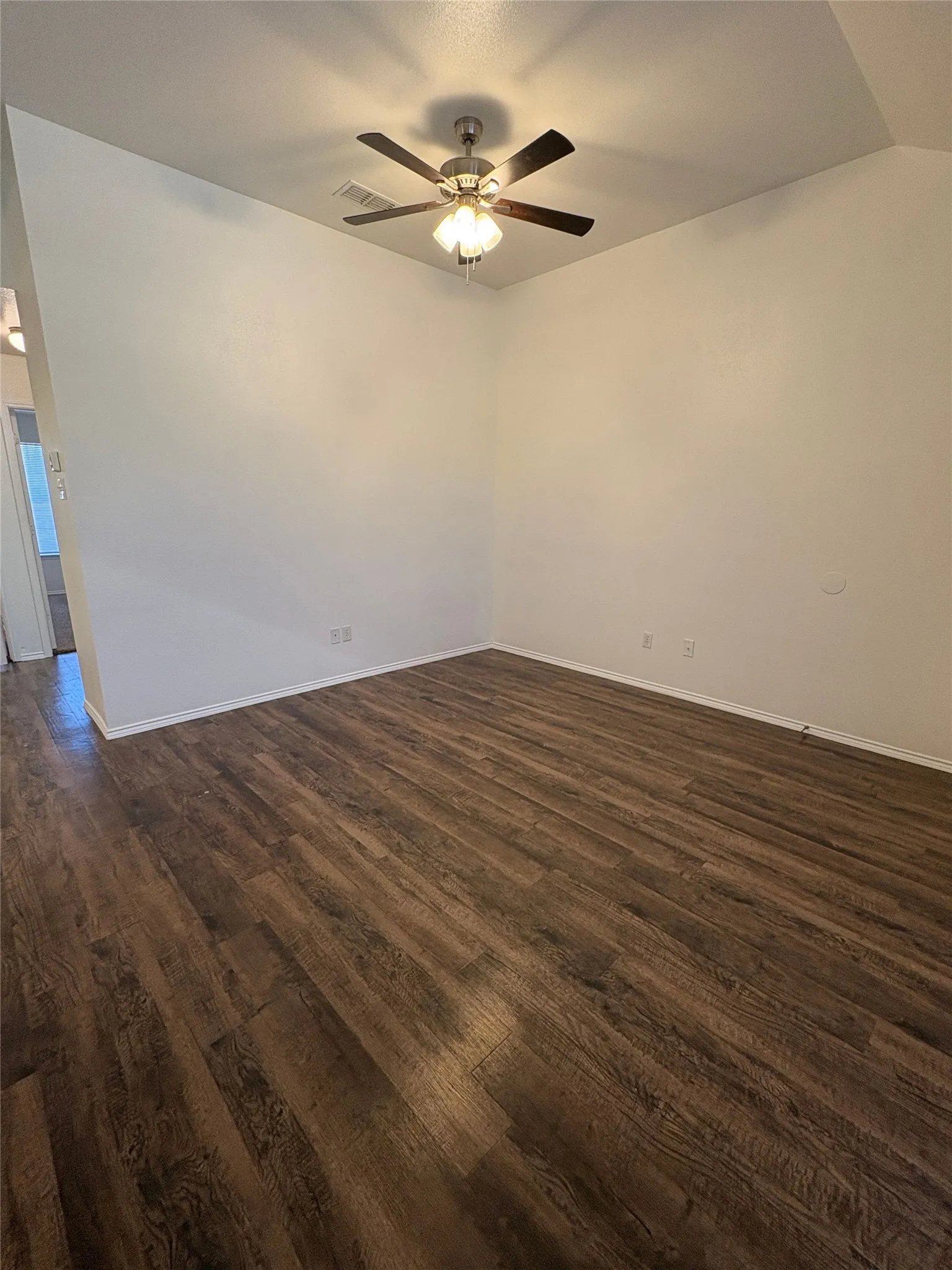 Wood-finish flooring with white wall finishes and a ceiling fan with integrated lighting