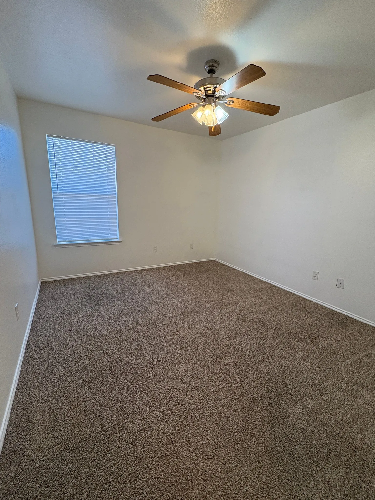 Textured carpeting, neutral wall tones, window with horizontal blinds, sloped ceiling, and a ceiling fan with light fixture