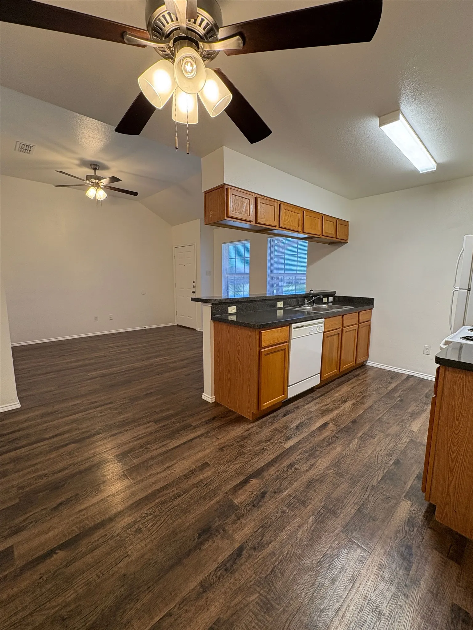 Wood-finish flooring throughout, vaulted ceiling, recessed lighting, and kitchen with wood cabinetry and dark countertops