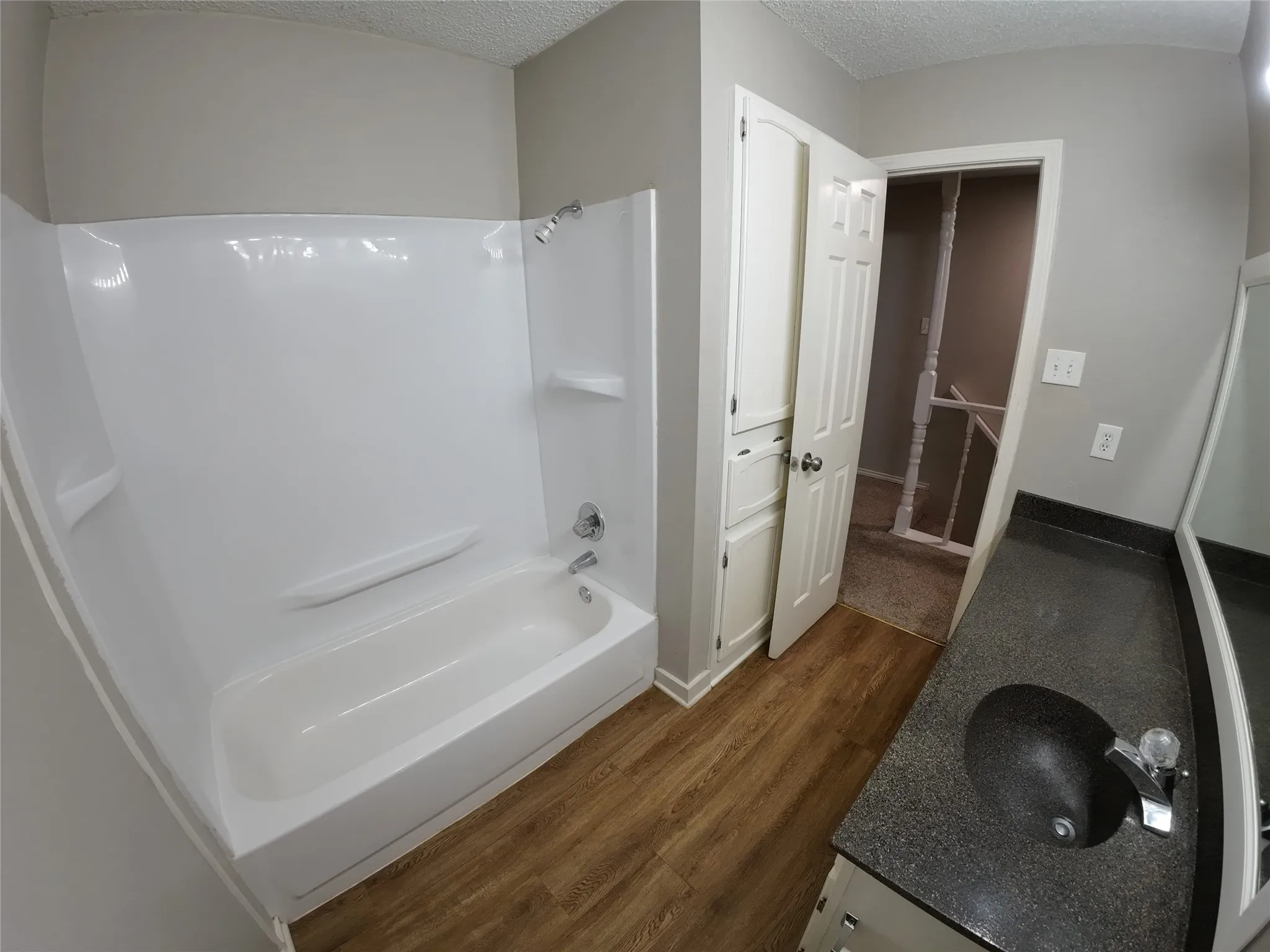 Bathroom featuring a full tub and shower combination, dark speckled countertop with an undermount sink, built-in cabinetry, wood-finish flooring, and light gray walls