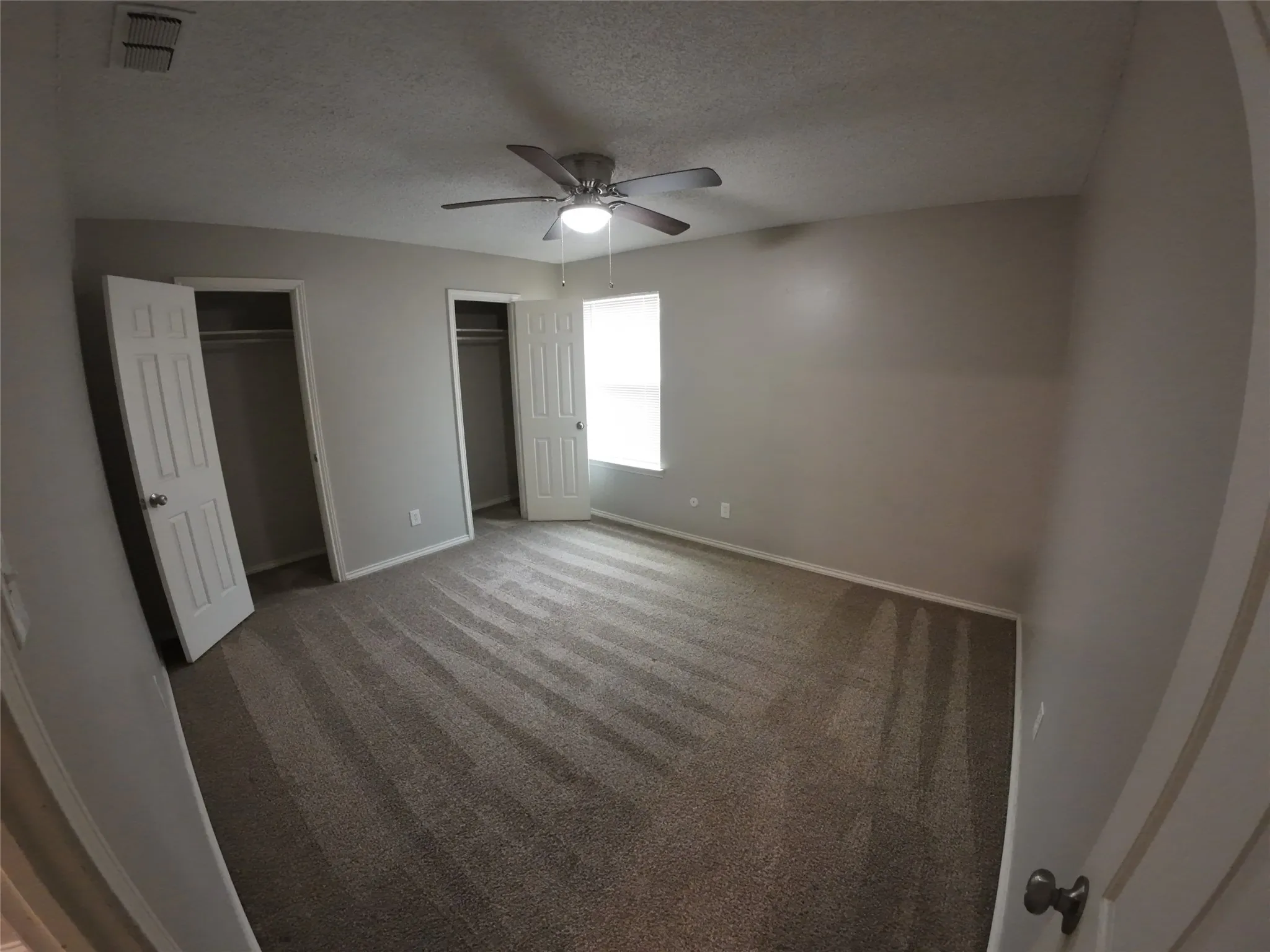 Carpeted room with neutral wall tones, a ceiling fan with integrated lighting, and two closets featuring white bi-fold doors
