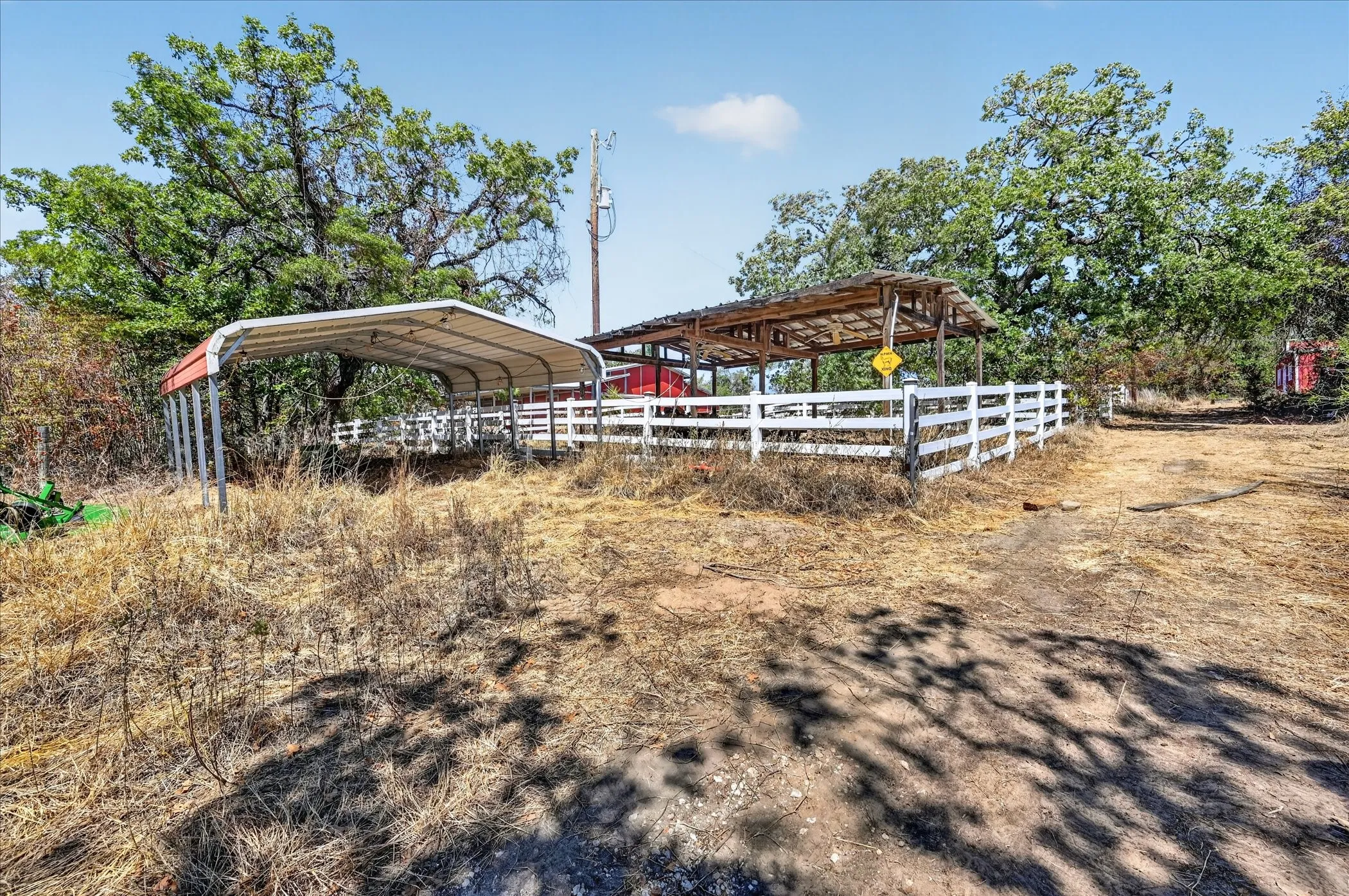 Metal carport structure, white fencing, and a wooden-framed covered structure