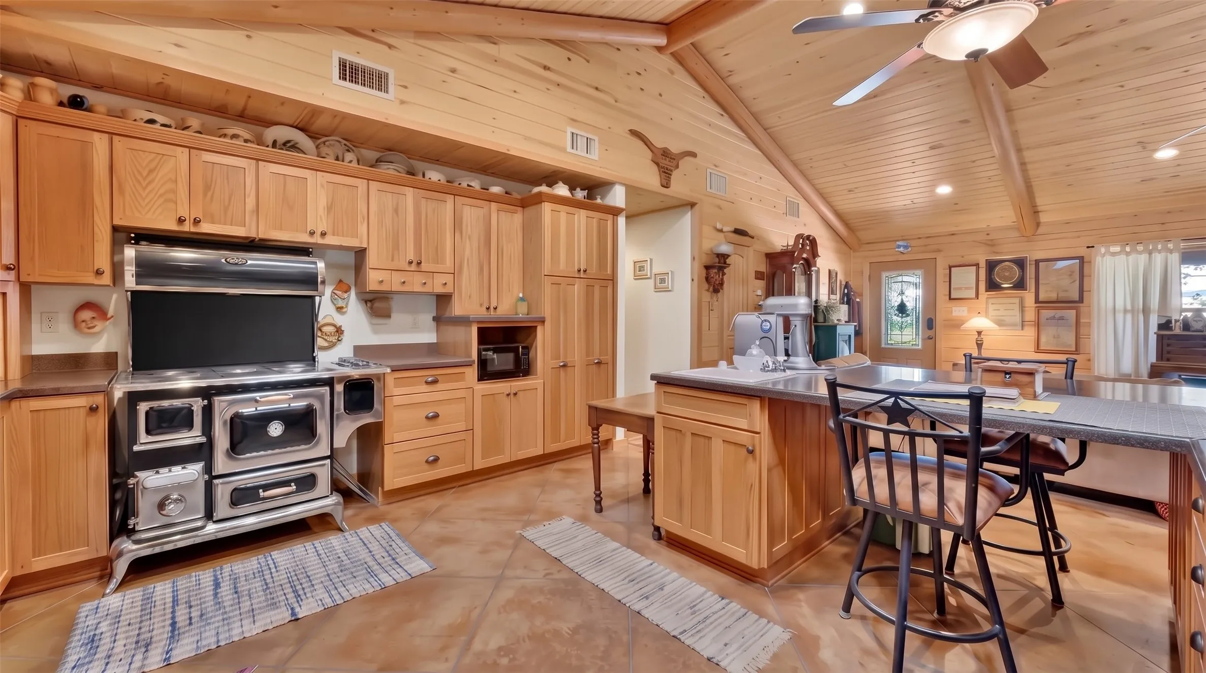 Vaulted wood-paneled ceiling, wood-finish cabinetry, built-in range, island with built-in storage, and tile flooring